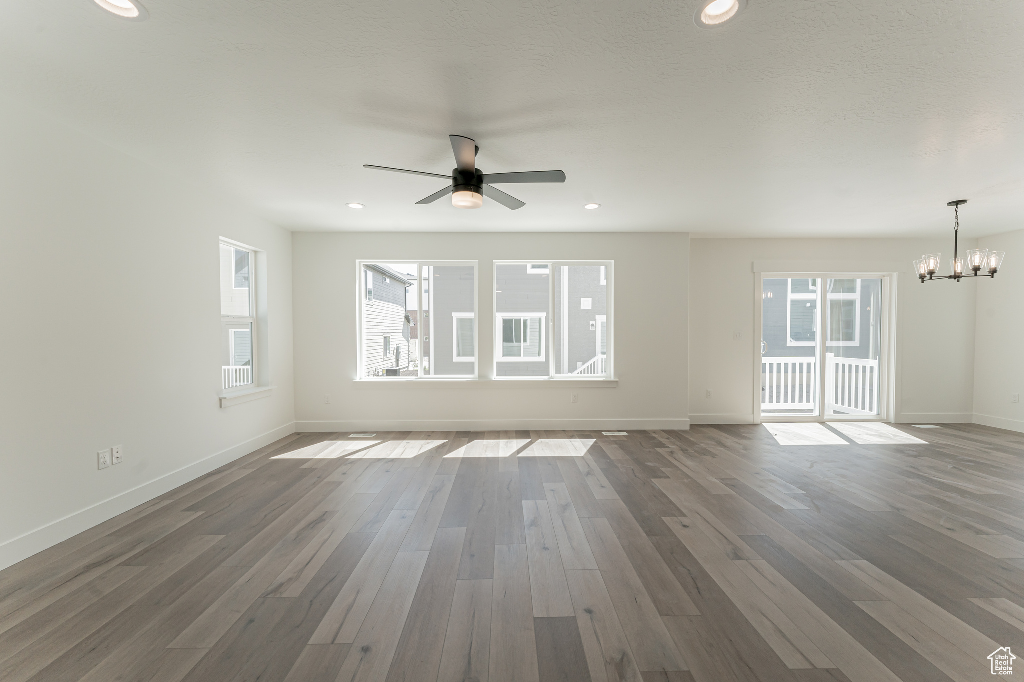 Unfurnished living room featuring ceiling fan with notable chandelier and dark hardwood / wood-style floors