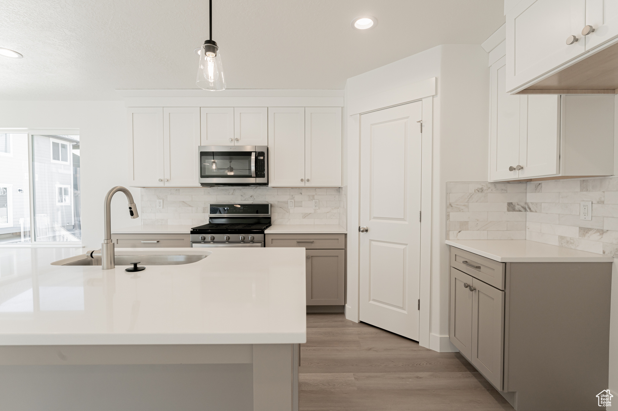 Kitchen with decorative backsplash, light hardwood / wood-style floors, pendant lighting, and stainless steel appliances