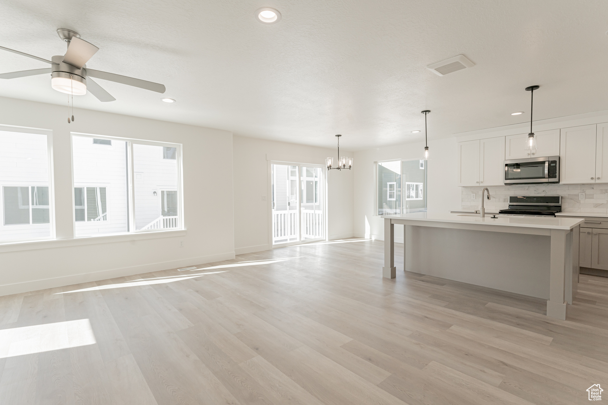 Kitchen featuring light hardwood / wood-style floors, decorative backsplash, a center island with sink, range, and ceiling fan with notable chandelier