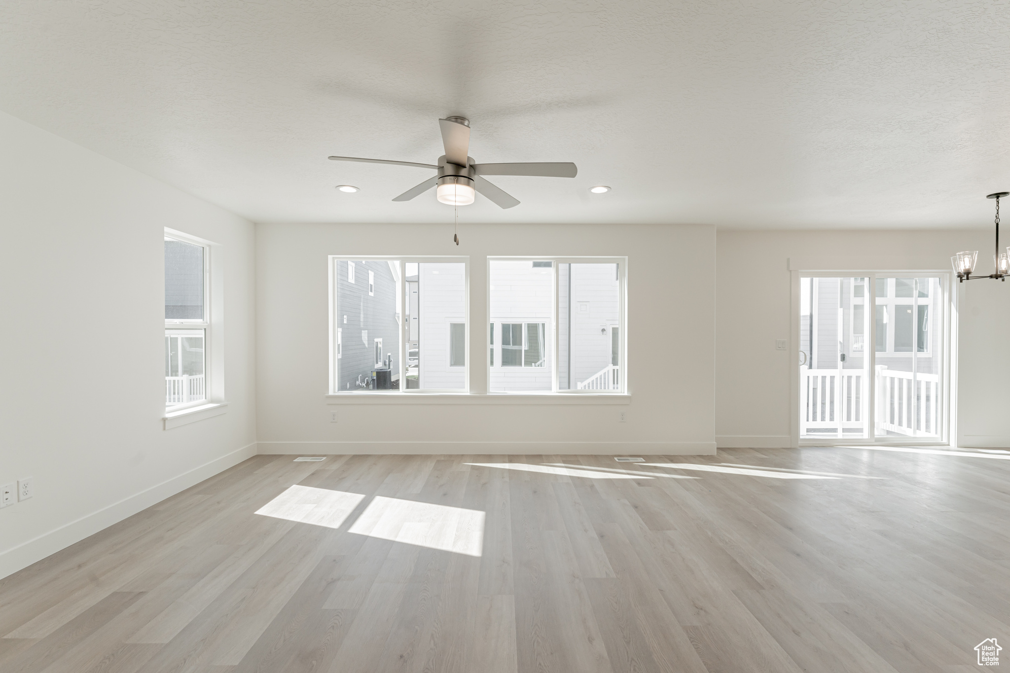 Spare room featuring ceiling fan with notable chandelier and light hardwood / wood-style flooring