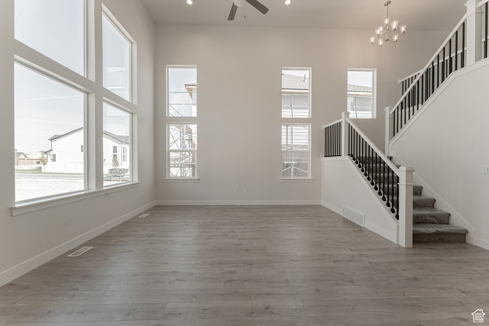 Unfurnished living room featuring hardwood / wood-style floors, ceiling fan with notable chandelier, plenty of natural light, and a towering ceiling