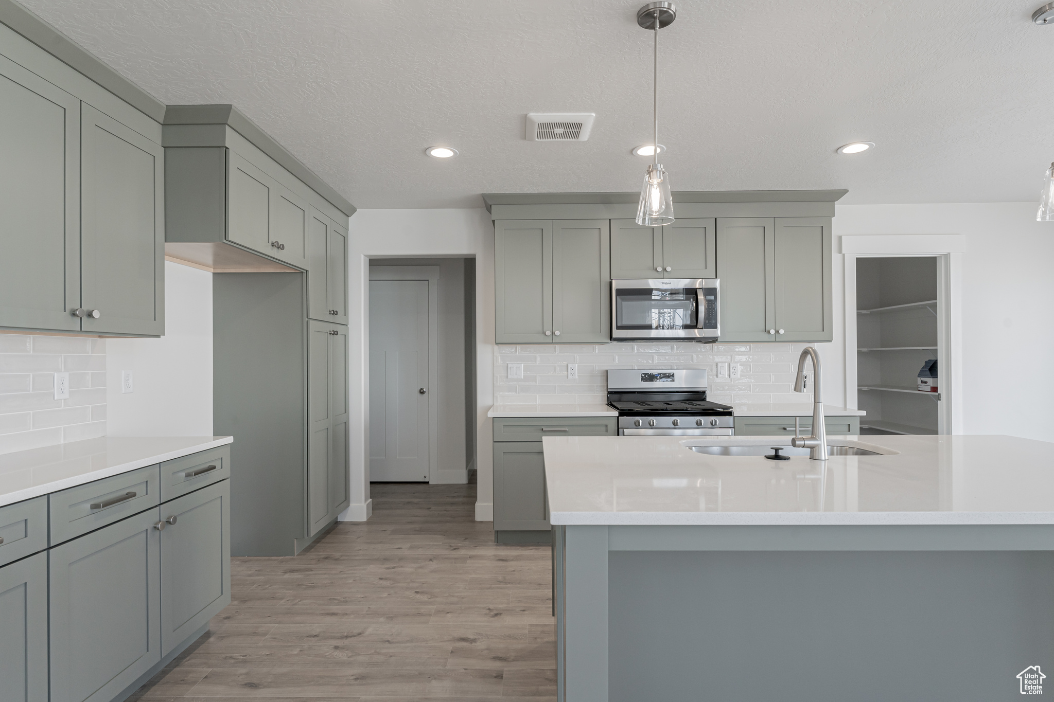 Kitchen with pendant lighting, appliances with stainless steel finishes, a kitchen island with sink, sink, and light wood-type flooring