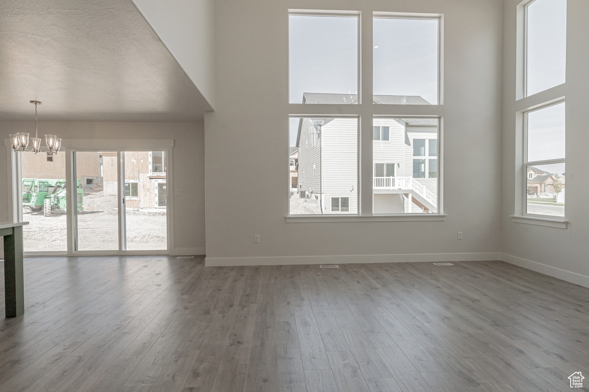 Unfurnished living room with a wealth of natural light, a notable chandelier, wood-type flooring, and a towering ceiling