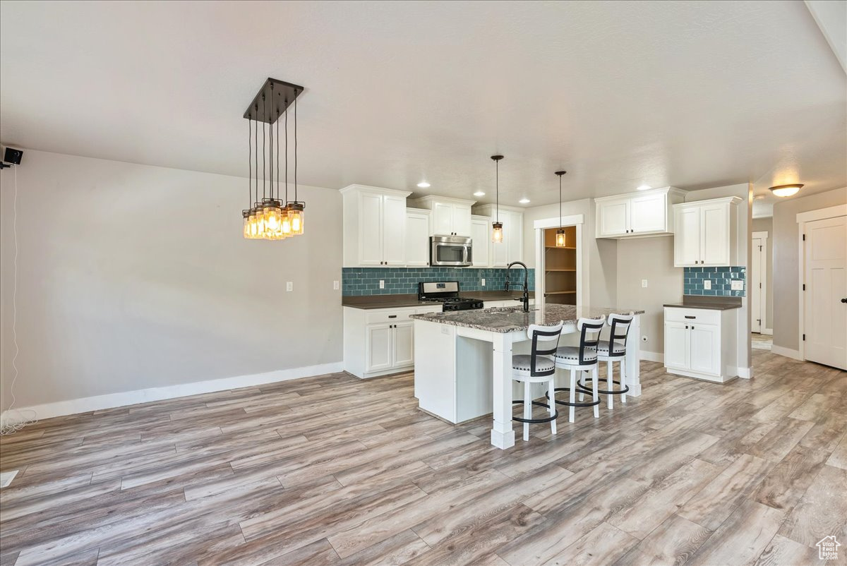 Kitchen with decorative light fixtures, light hardwood / wood-style floors, a center island with sink, range with gas cooktop, and white cabinets