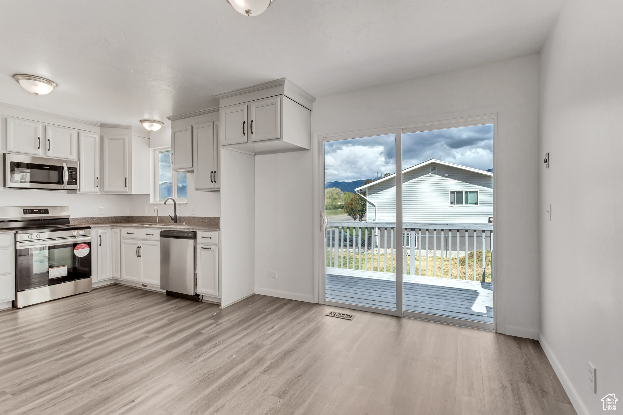 Kitchen with a healthy amount of sunlight, appliances with stainless steel finishes, white cabinets, and light wood-type flooring