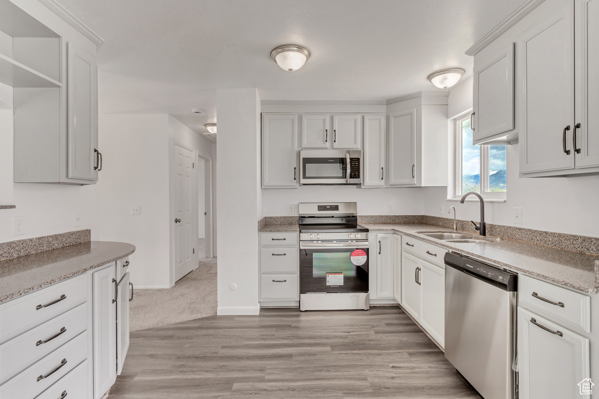 Kitchen featuring light colored carpet, white cabinetry, appliances with stainless steel finishes, light stone counters, and sink