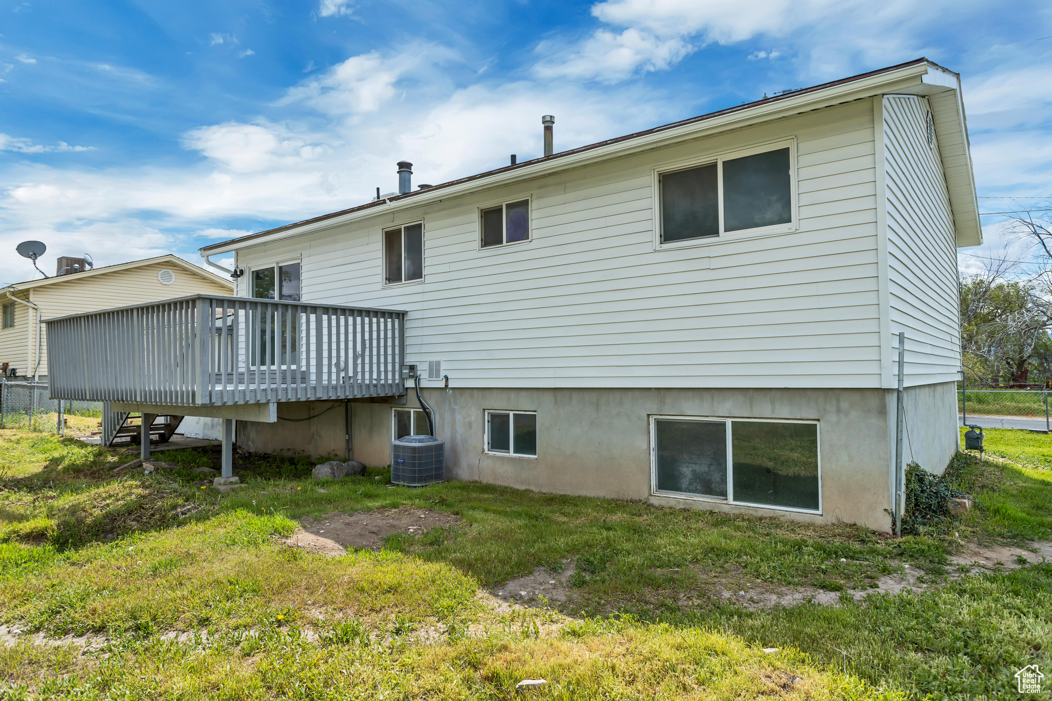 Rear view of house with central AC unit, a wooden deck, and a lawn