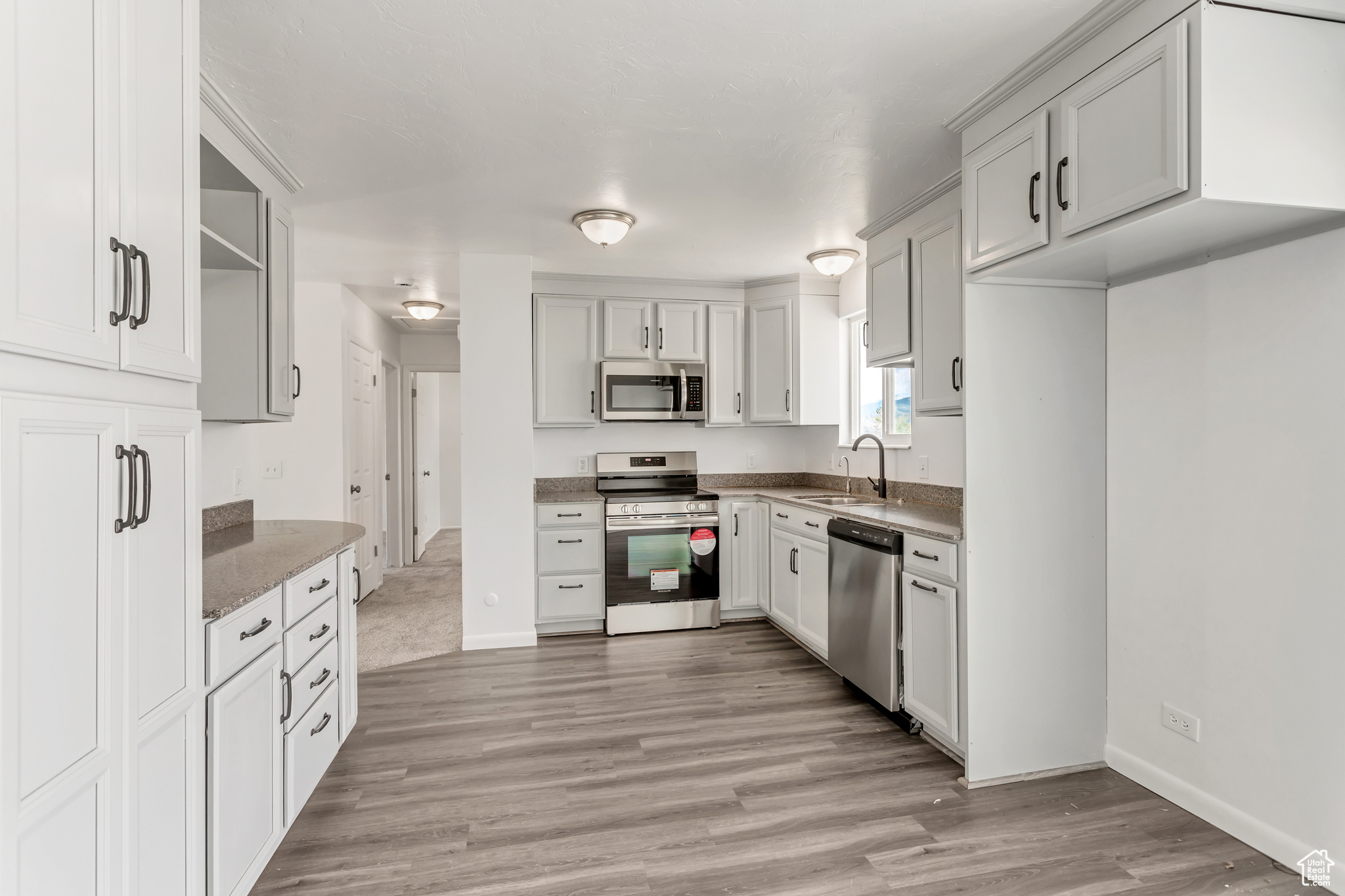 Kitchen with light hardwood / wood-style floors, appliances with stainless steel finishes, sink, and stone counters