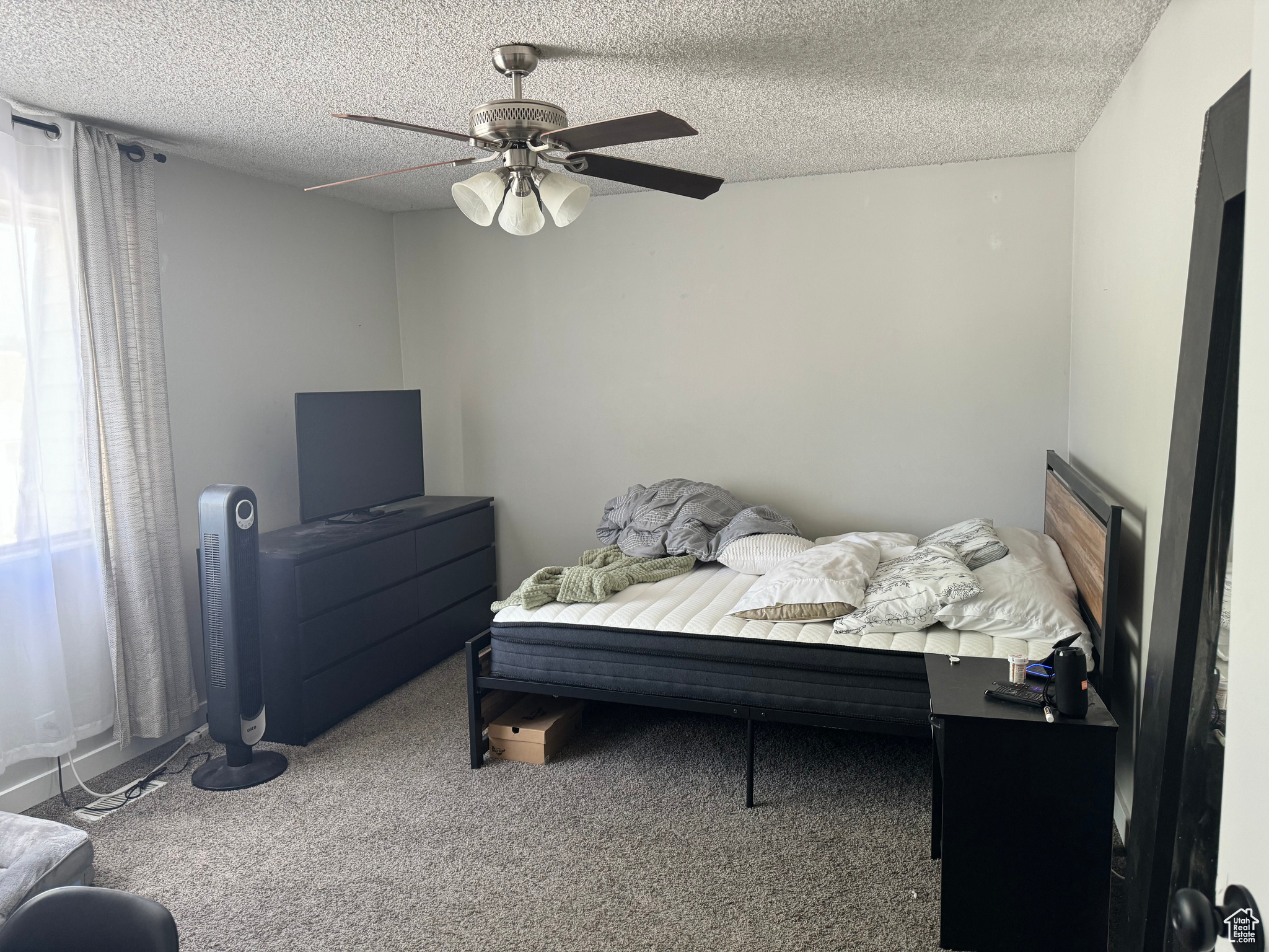 Carpeted bedroom with ceiling fan and a textured ceiling