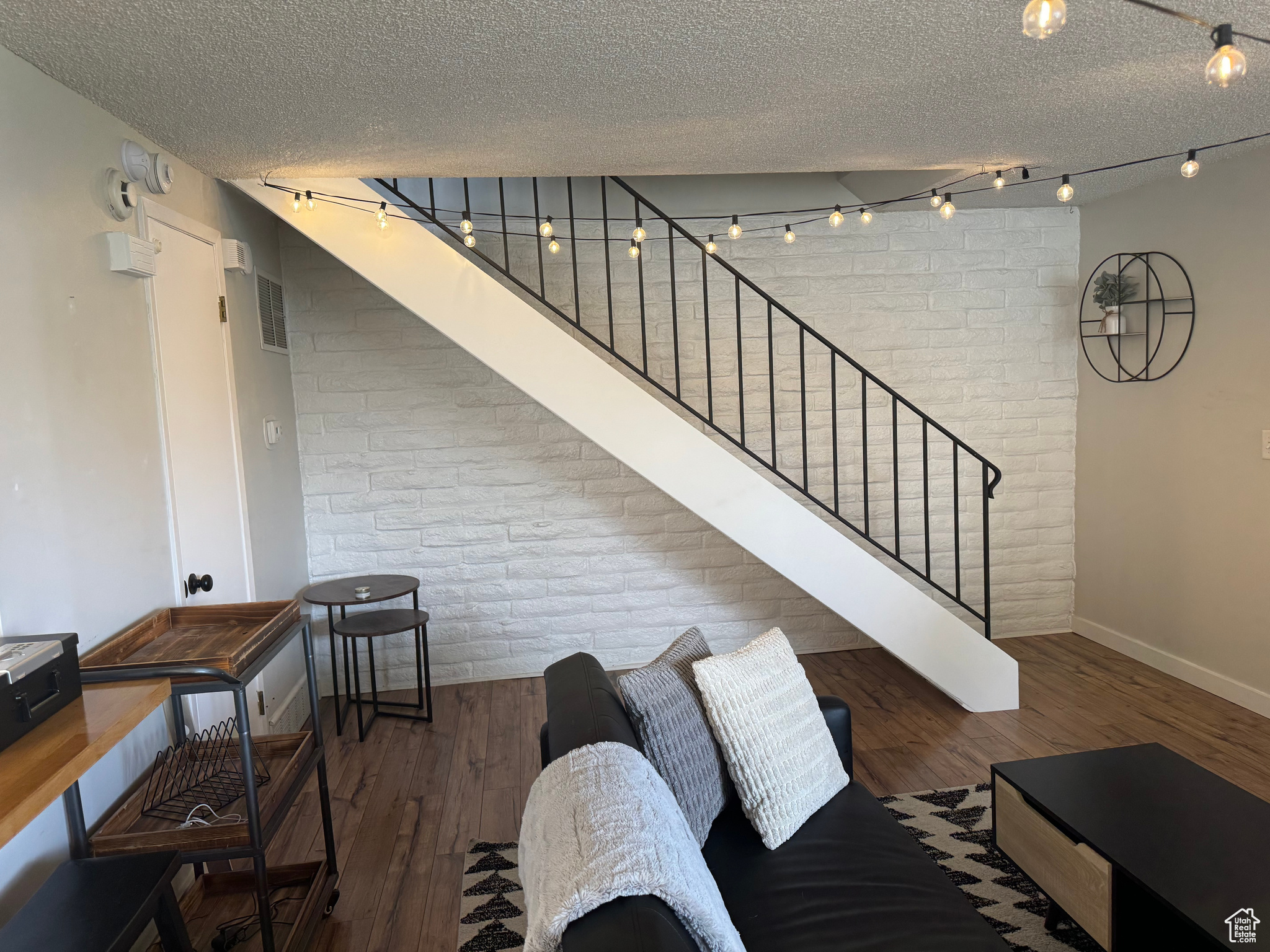 Living room with a textured ceiling, dark hardwood / wood-style flooring, brick wall, and track lighting