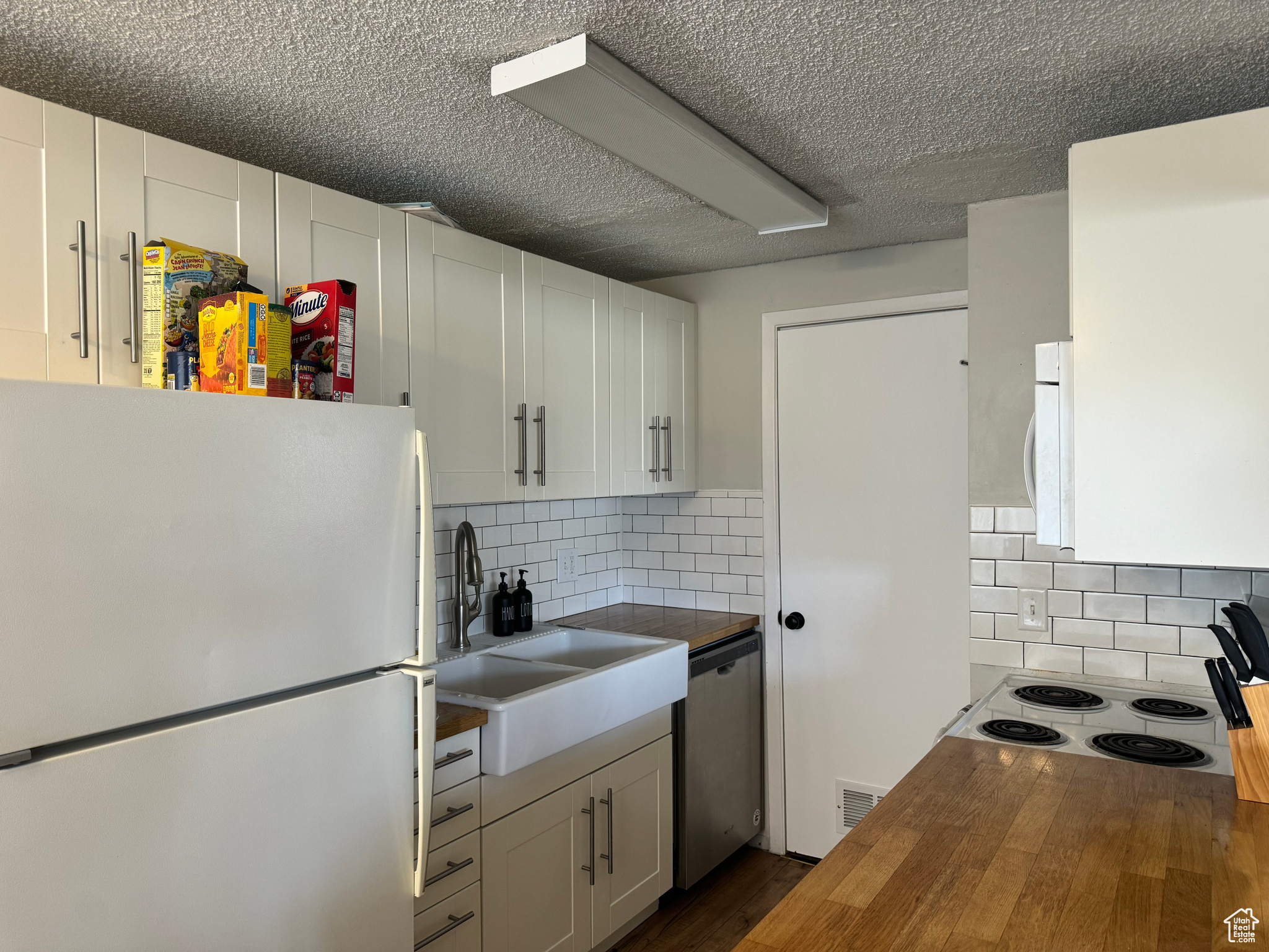 Kitchen featuring backsplash, butcher block countertops, white appliances, and white cabinetry