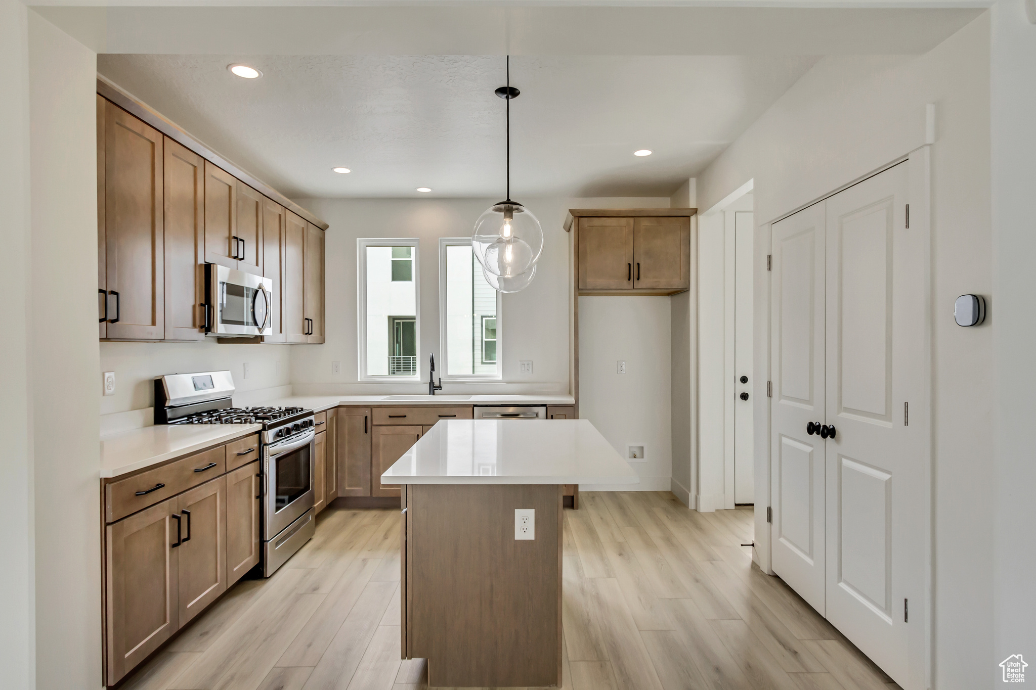 Kitchen with a center island, stainless steel appliances, light hardwood / wood-style floors, and decorative light fixtures