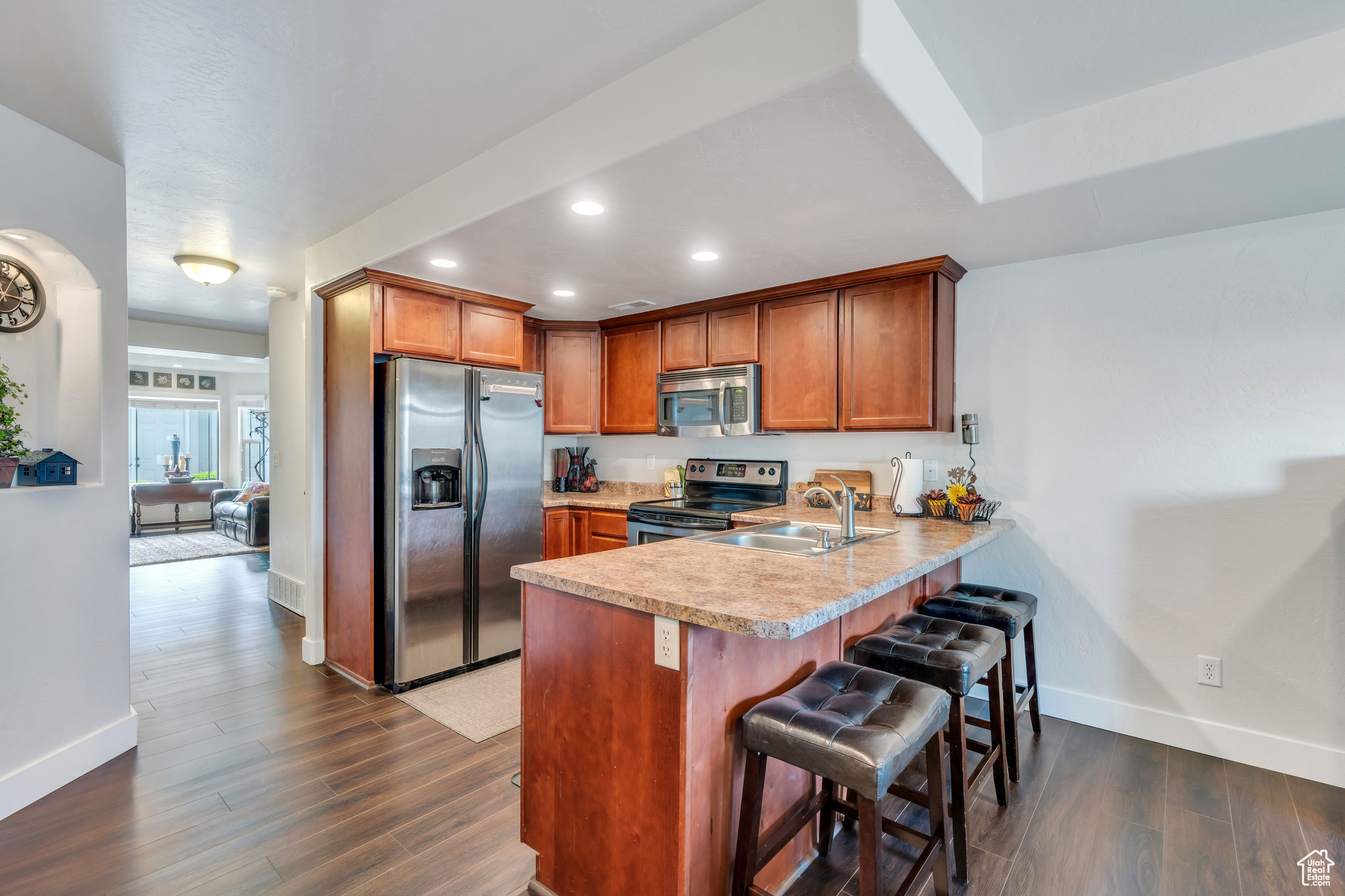 Kitchen with appliances with stainless steel finishes, dark hardwood / wood-style floors, a breakfast bar area, kitchen peninsula, and sink