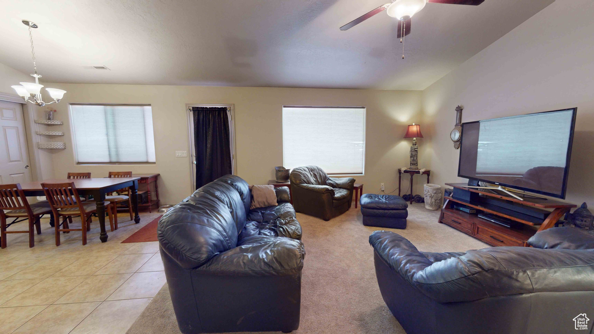 Tiled living room with ceiling fan with notable chandelier and a healthy amount of sunlight