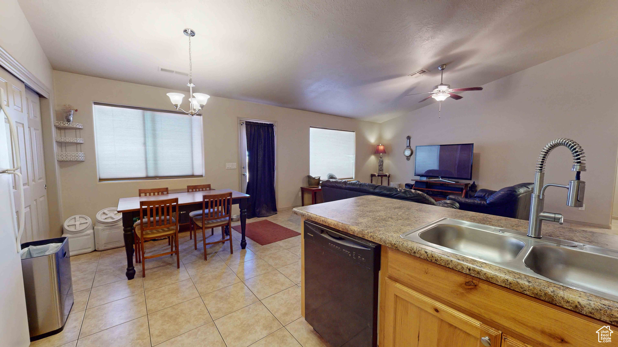 Kitchen featuring ceiling fan with notable chandelier, black dishwasher, pendant lighting, sink, and light tile floors