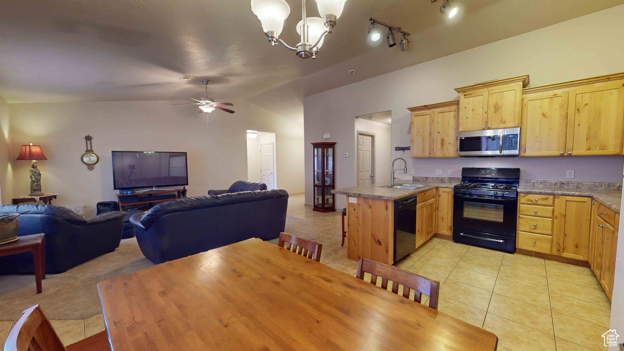 Kitchen featuring vaulted ceiling, black appliances, track lighting, sink, and light tile floors