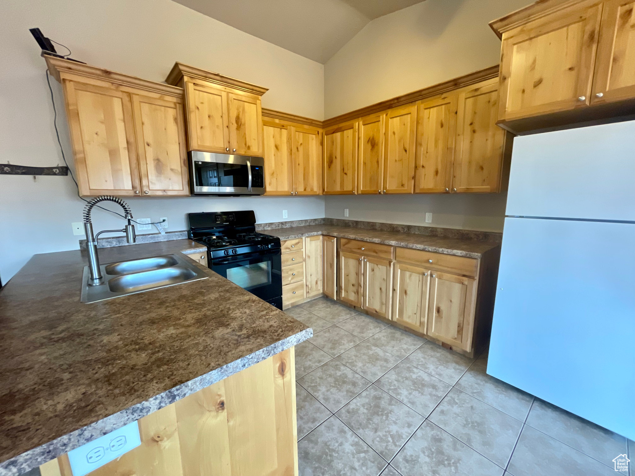 Kitchen with sink, white fridge, light tile patterned flooring, and black range with gas cooktop