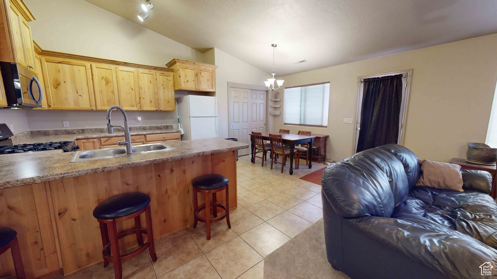 Kitchen featuring lofted ceiling, white refrigerator, range, sink, and light tile floors