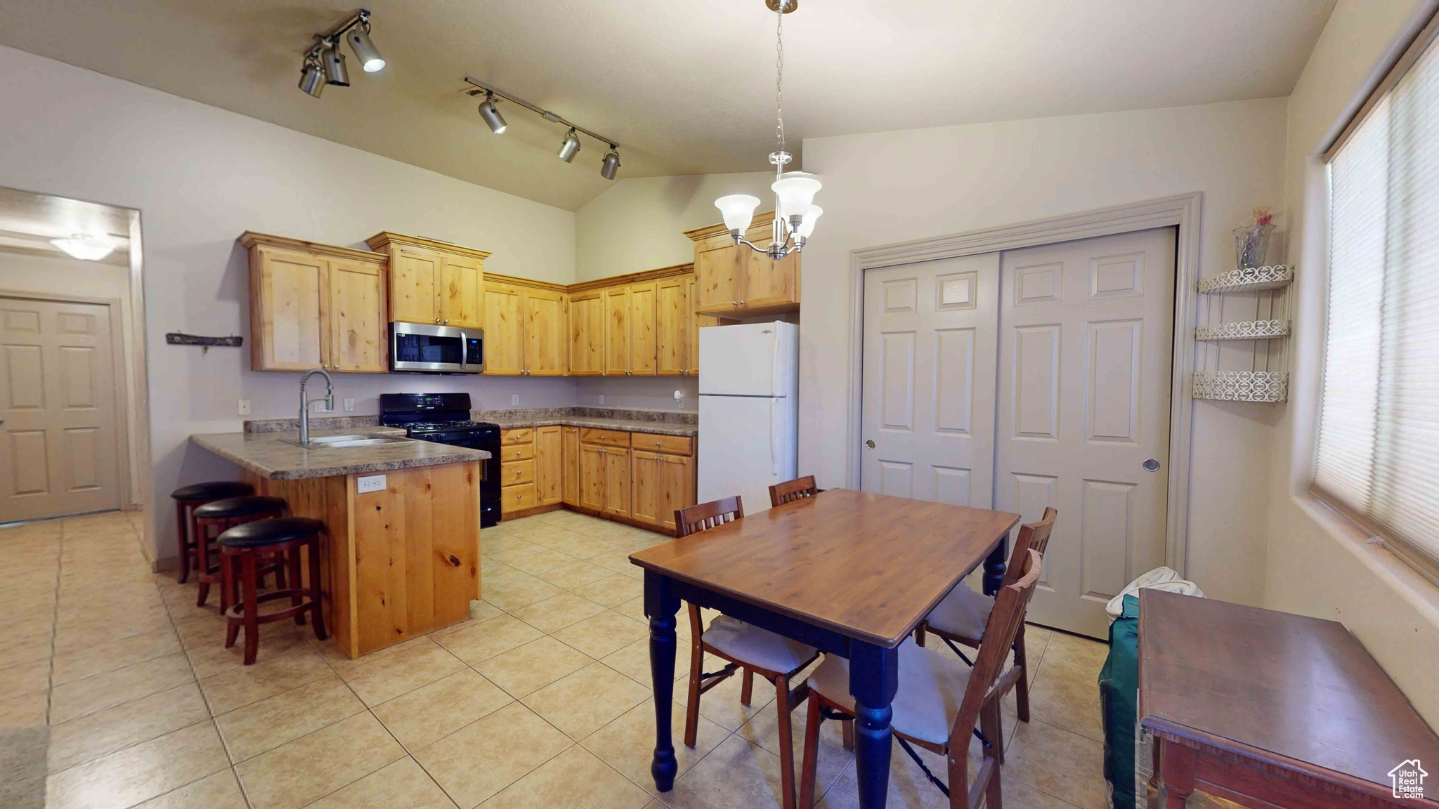 Kitchen featuring white fridge, black range oven, track lighting, sink, and light tile floors