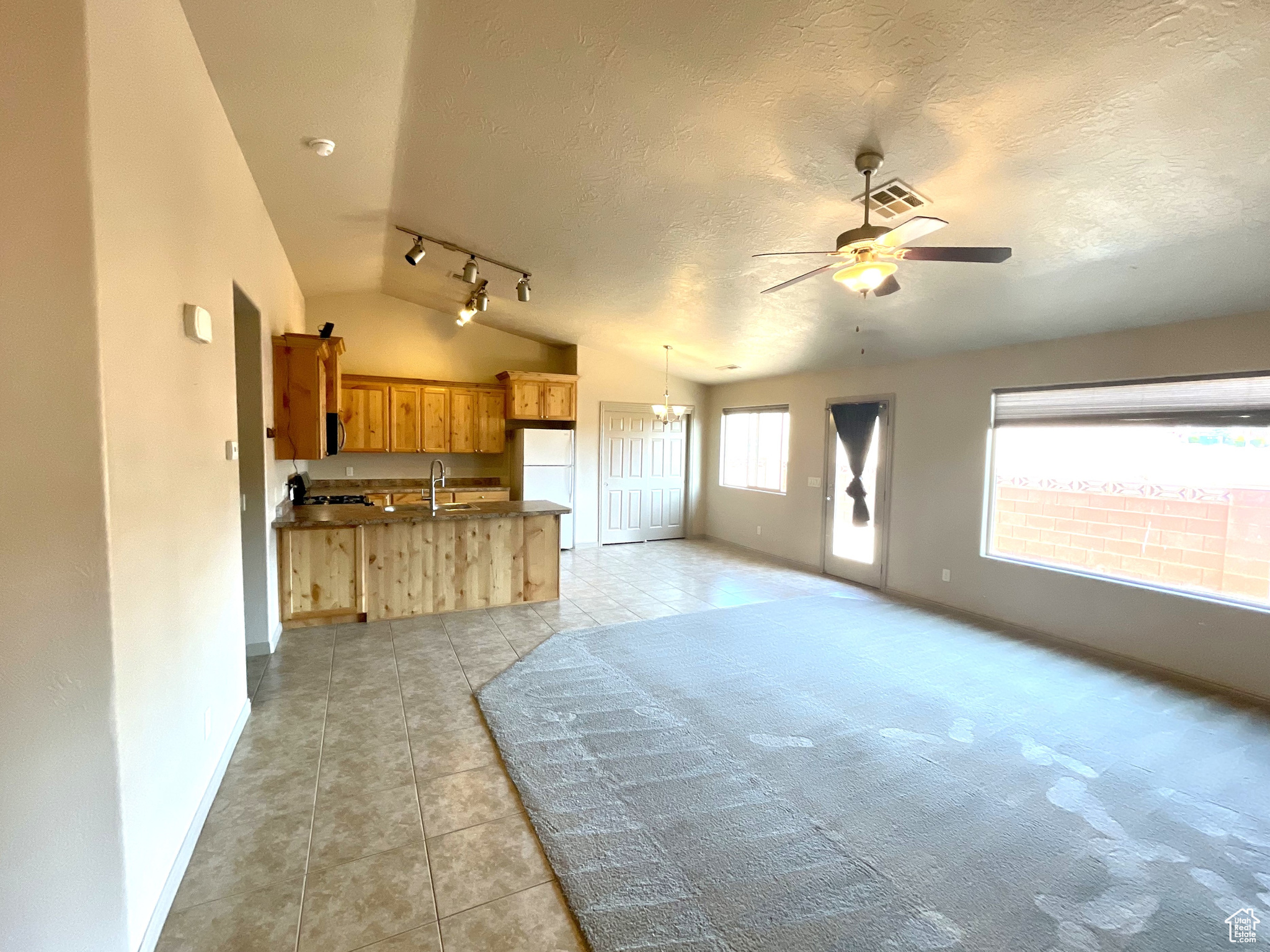 Living room featuring a textured ceiling, rail lighting, sink, ceiling fan, and vaulted ceiling