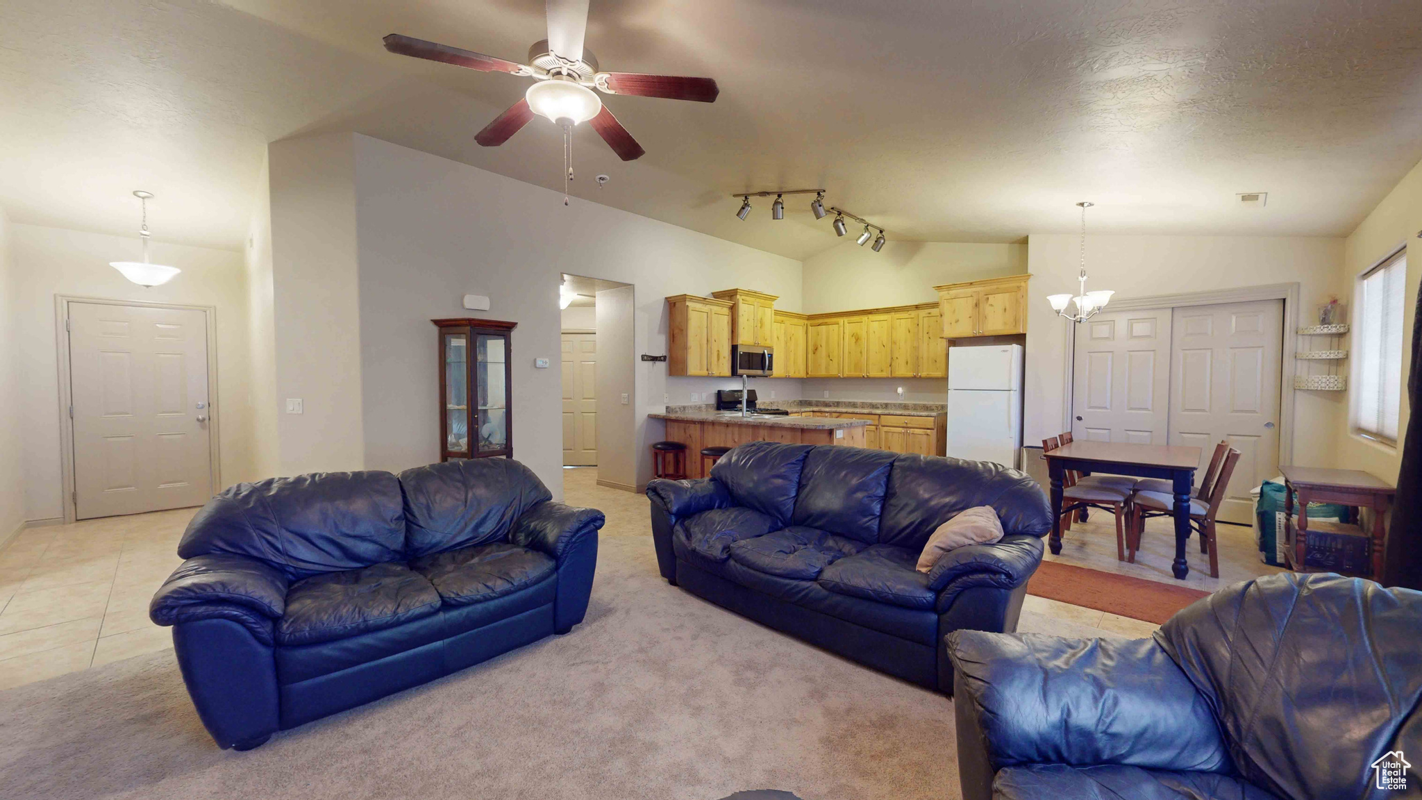 Carpeted living room with ceiling fan with notable chandelier, rail lighting, and lofted ceiling