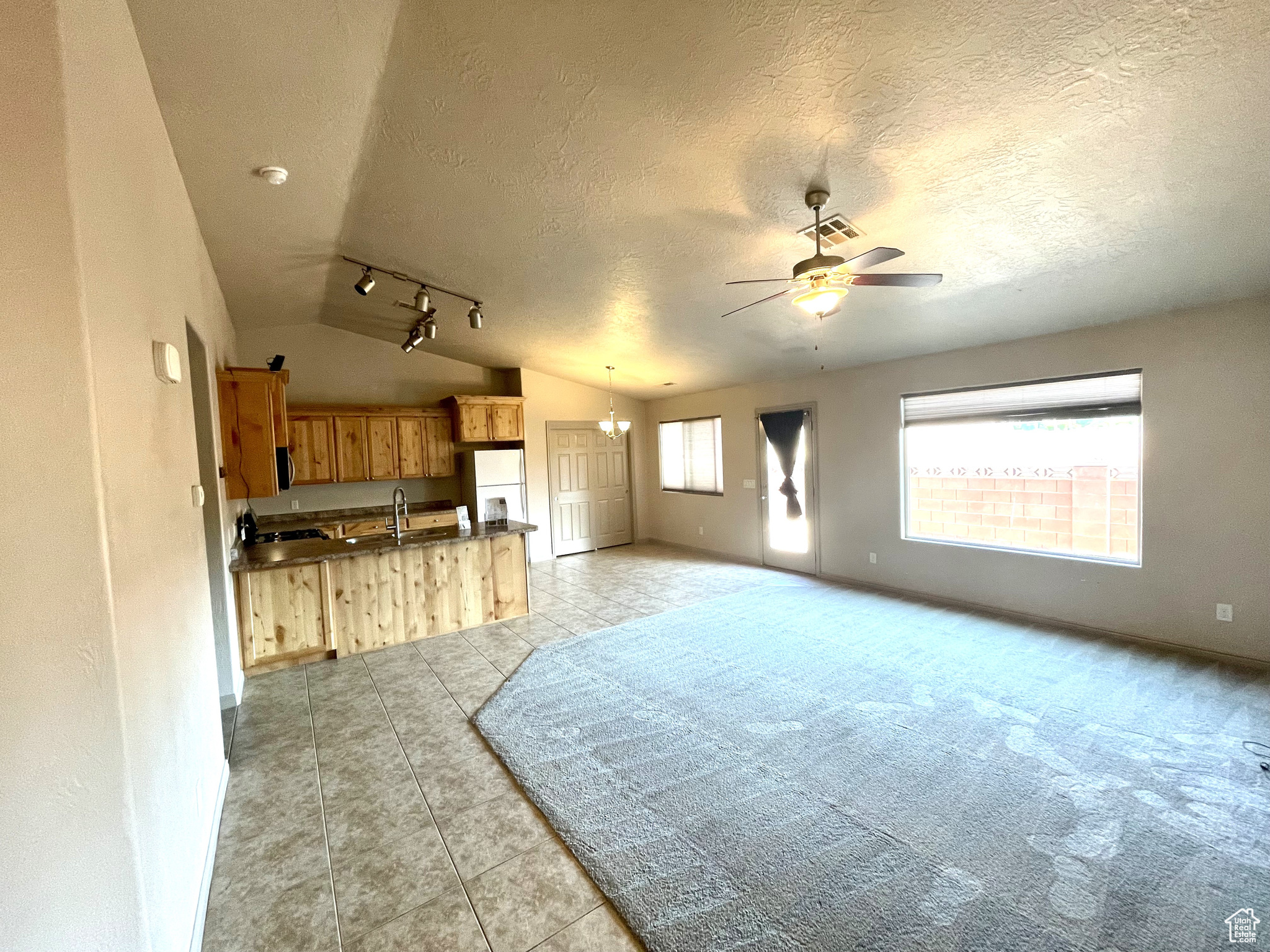 Tiled living room with lofted ceiling, track lighting, a wealth of natural light, and ceiling fan