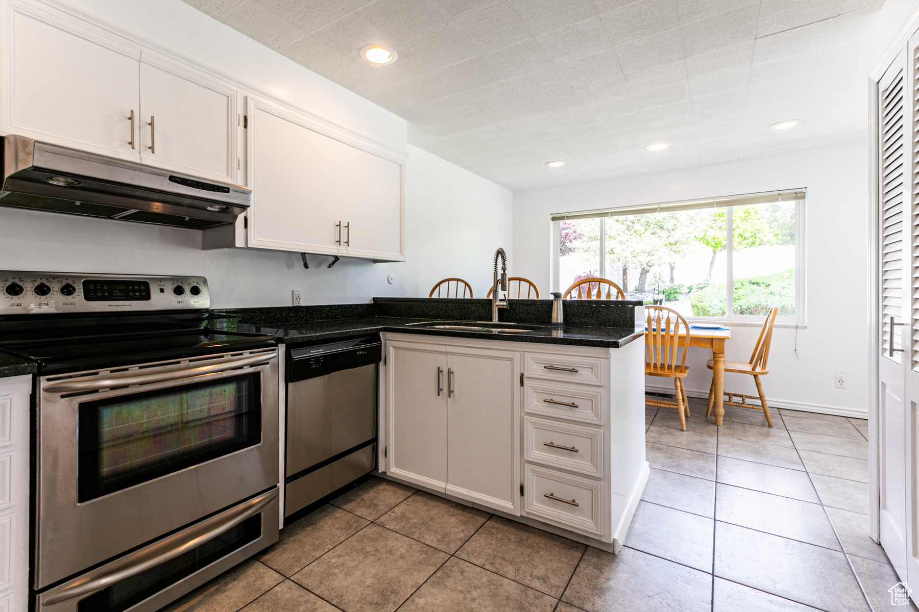 Kitchen featuring white cabinets, appliances with stainless steel finishes, granite countertops, and light tile floors