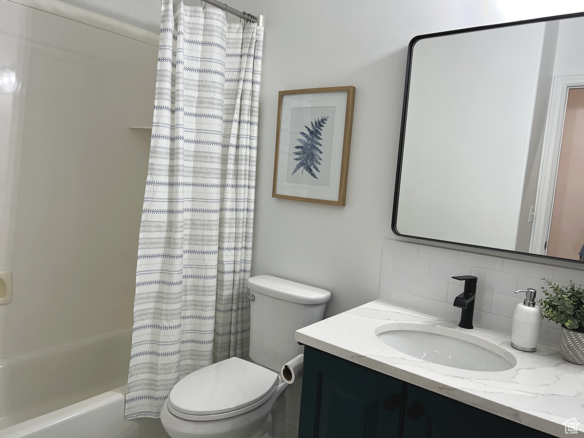 Full bathroom with backsplash, shower / tub combo, vanity, and toilet