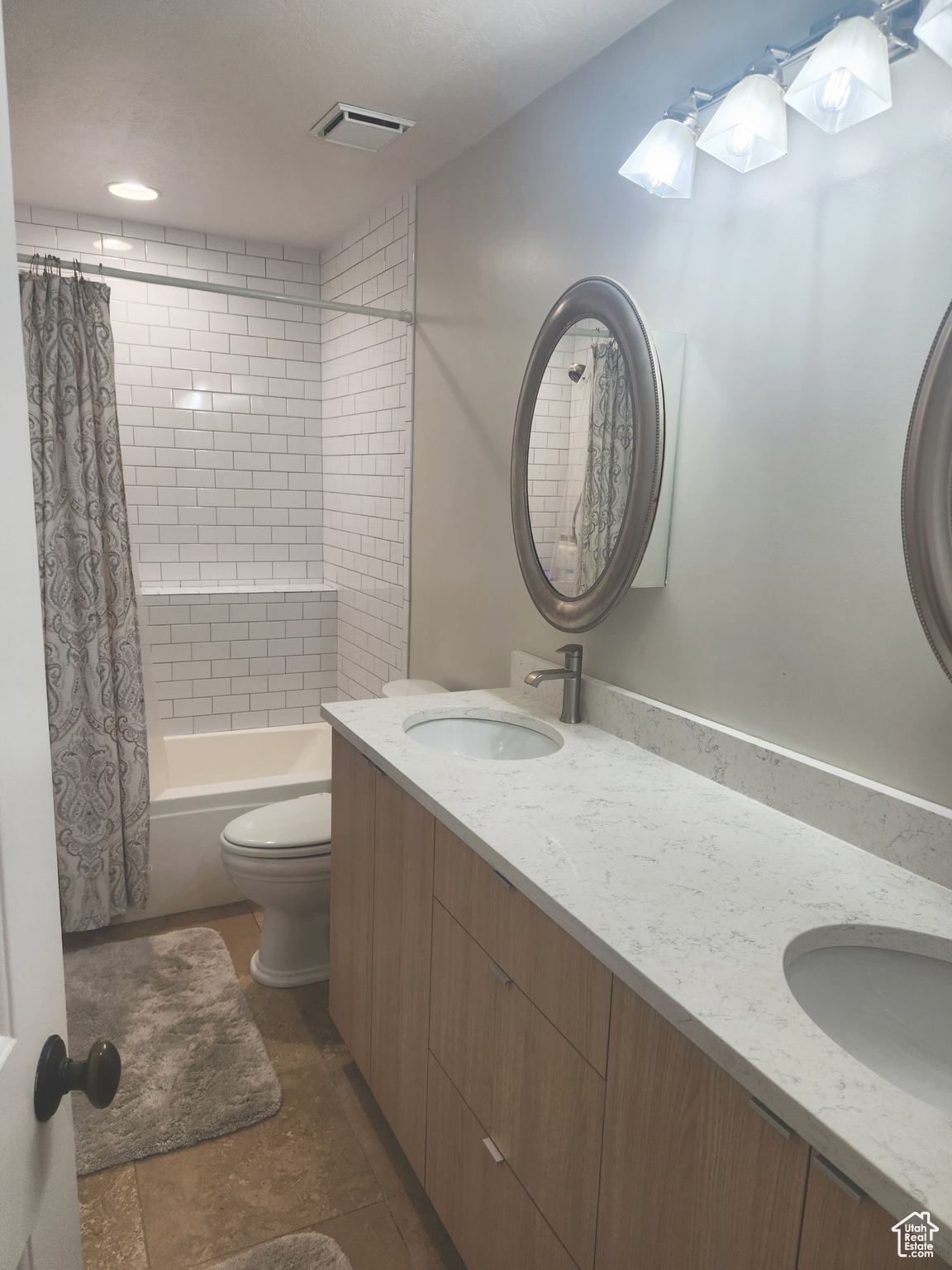 Full bathroom featuring tile floors, toilet, double vanity, and shower / bathtub combination with curtain