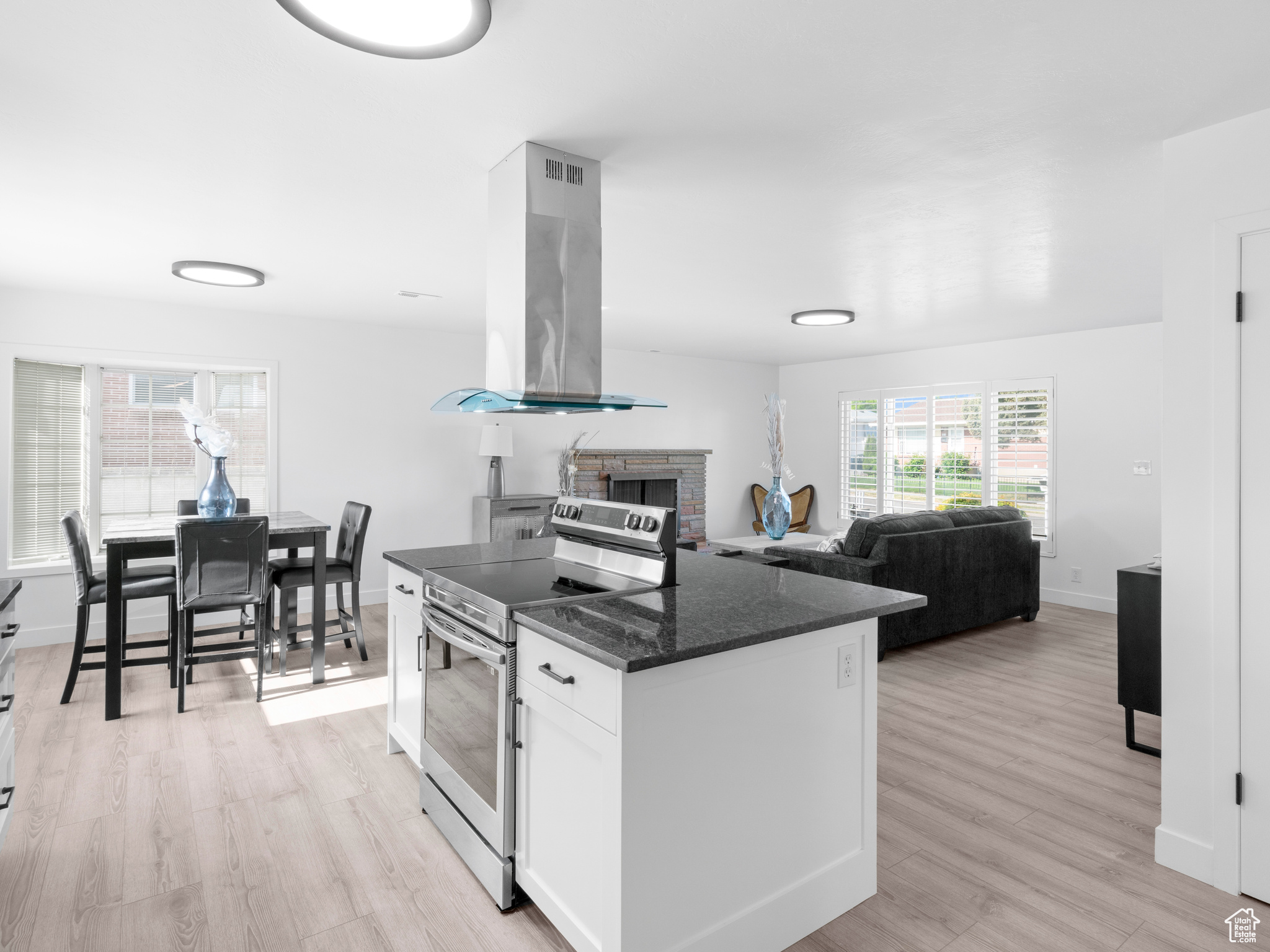 Kitchen featuring a fireplace, island range hood, light hardwood / wood-style flooring, white cabinets, and electric range