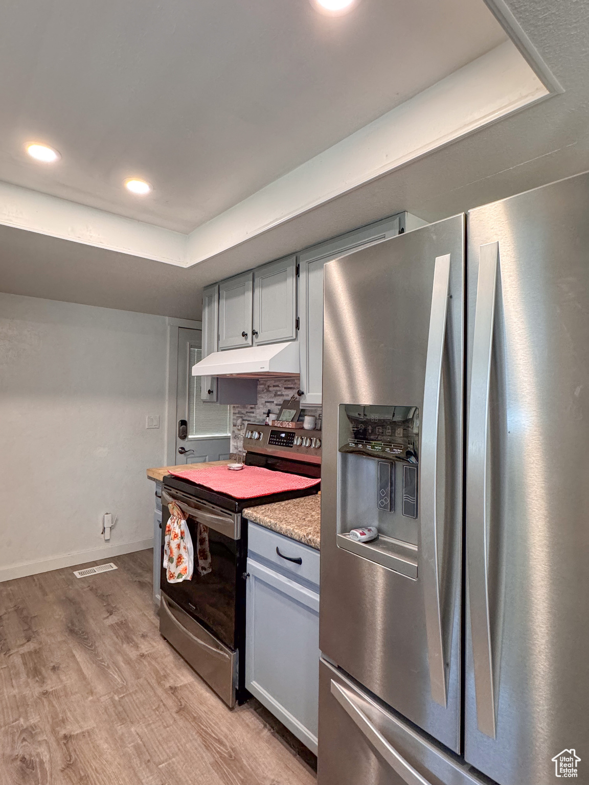 Kitchen with stainless steel refrigerator with ice dispenser, light hardwood / wood-style floors, backsplash, gray cabinetry, and electric range oven