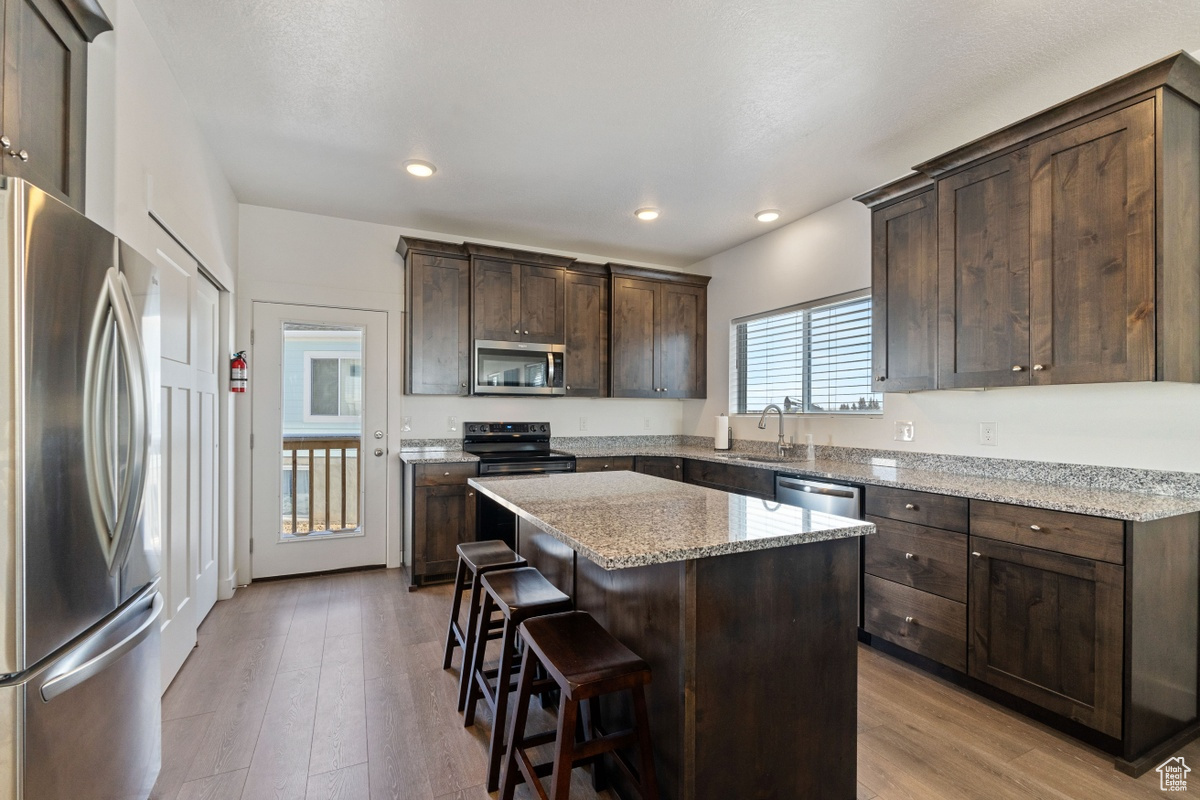 Kitchen with light stone counters, appliances with stainless steel finishes, a center island, and light hardwood / wood-style flooring