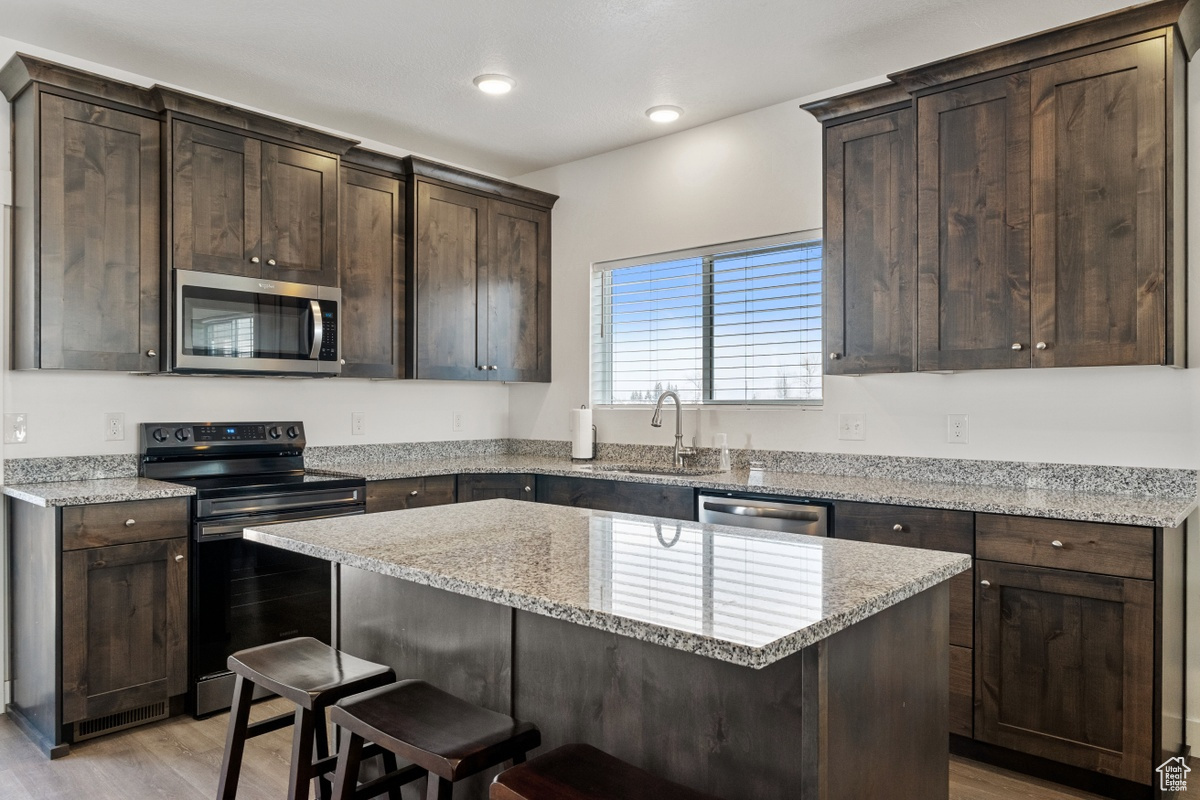 Kitchen featuring appliances with stainless steel finishes, light hardwood / wood-style floors, a center island, and sink