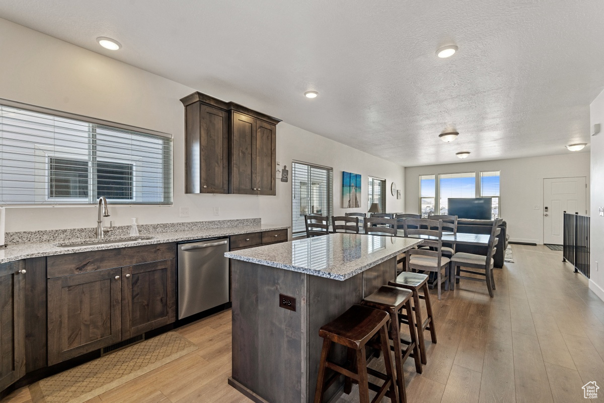 Kitchen with light stone countertops, light hardwood / wood-style floors, dishwasher, a kitchen island, and sink