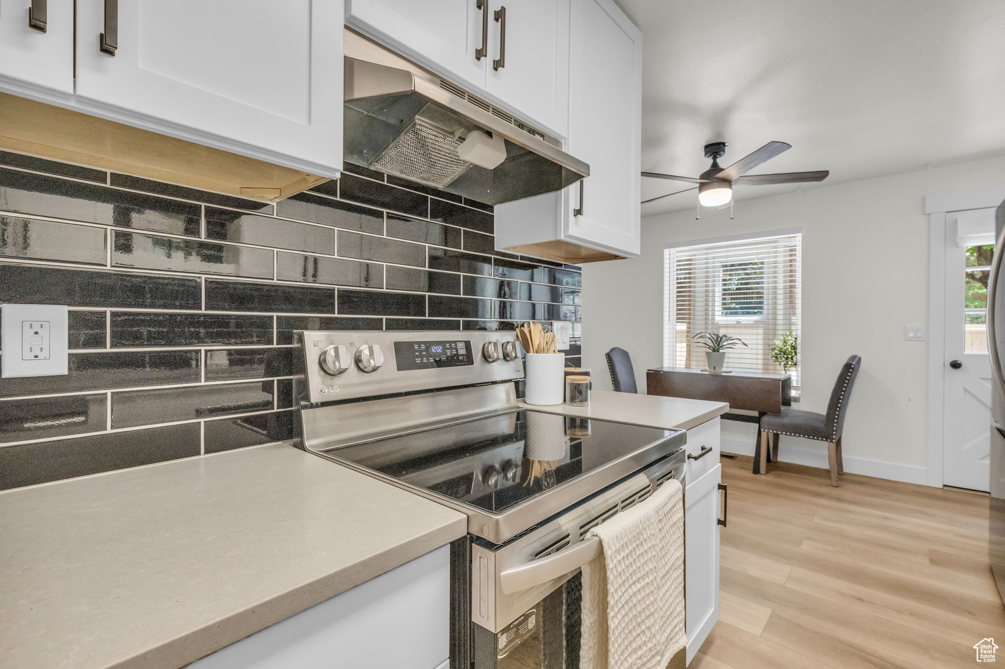 Kitchen with backsplash, stainless steel range with electric stovetop, white cabinetry, and light wood-type flooring