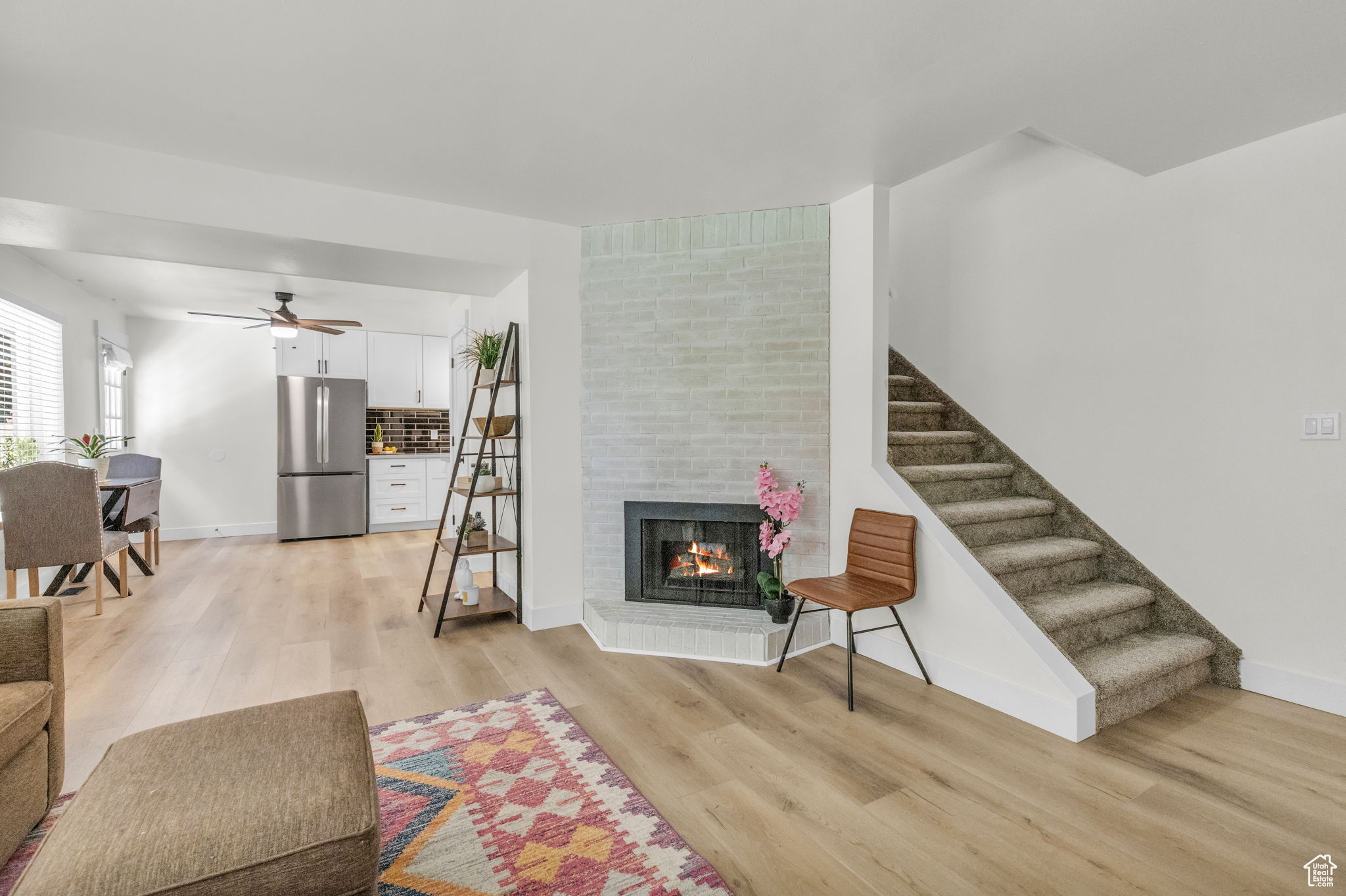 Living room with light hardwood / wood-style floors, brick wall, a brick fireplace, and ceiling fan