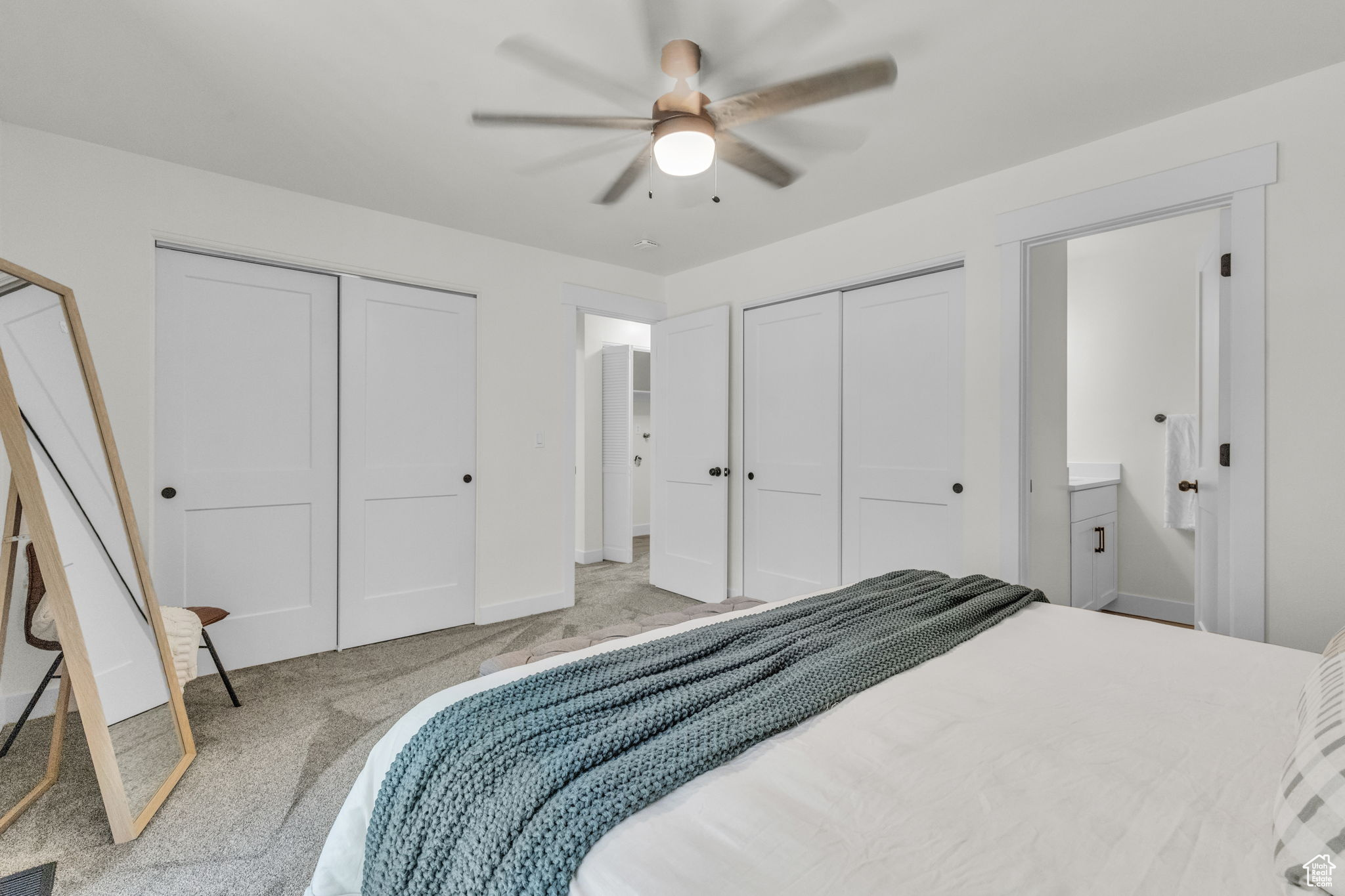 Carpeted bedroom featuring two closets, ceiling fan, and ensuite bath