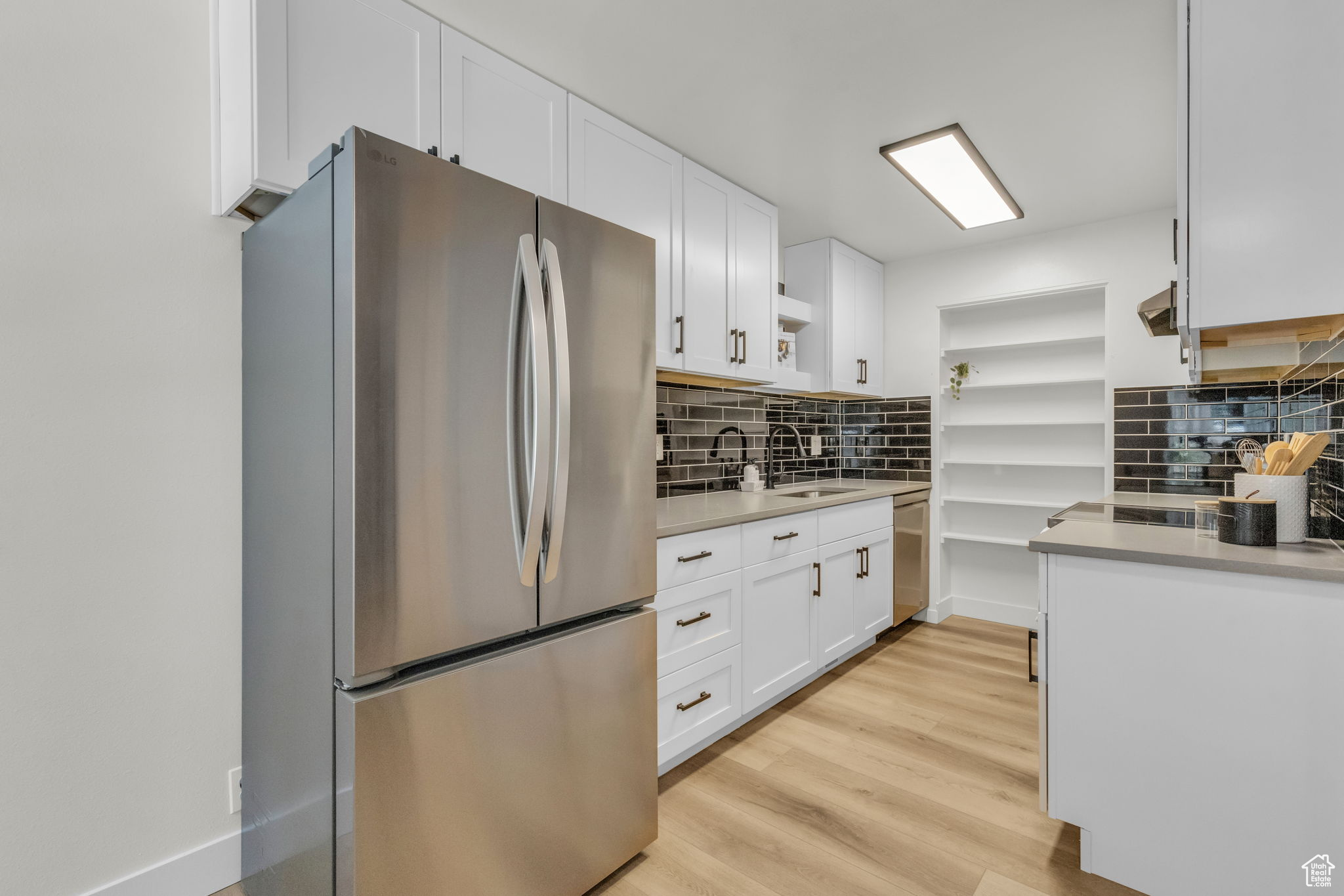 Kitchen with stainless steel appliances, backsplash, light wood-type flooring, white cabinets, and sink