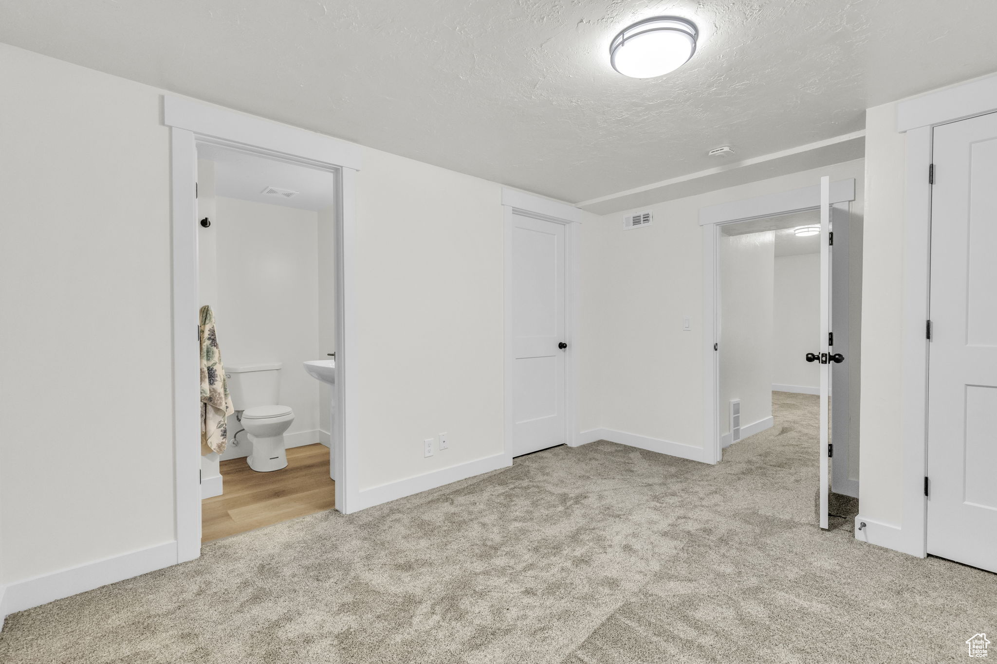 Unfurnished bedroom with a textured ceiling, a closet, light colored carpet, and connected bathroom