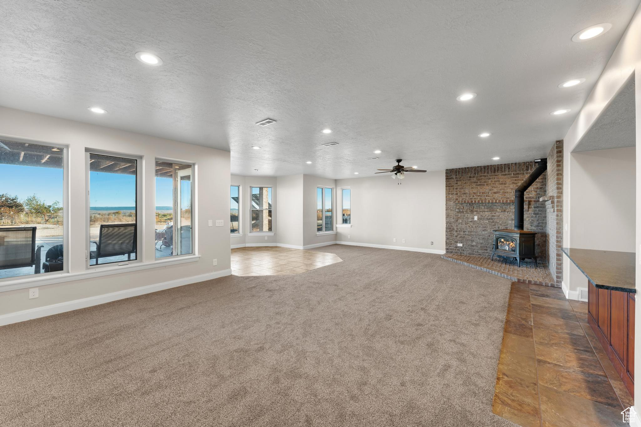 Living room featuring a wood stove, ceiling fan, a textured ceiling, and light carpet