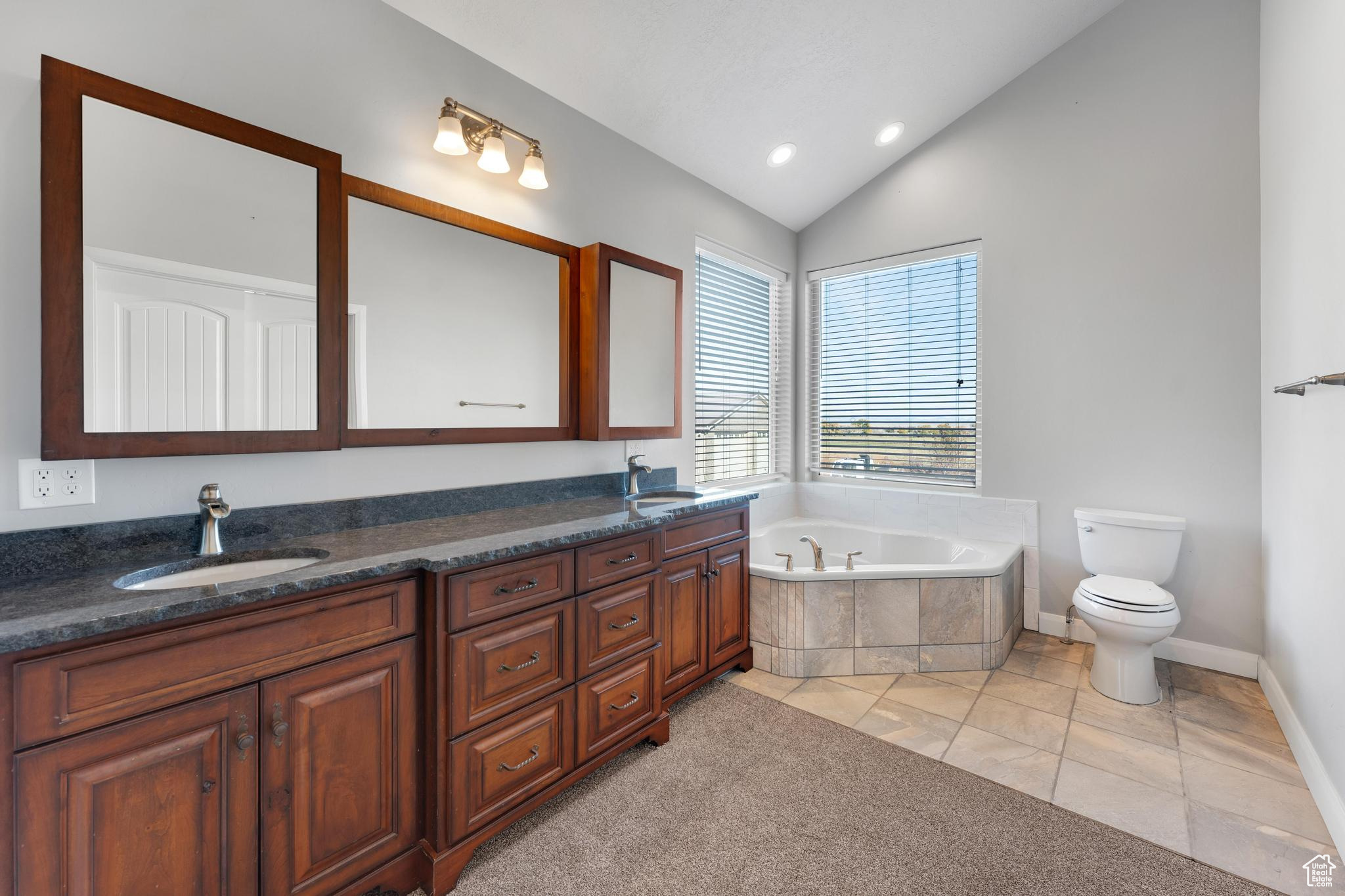 Master bathroom featuring lofted ceiling, dual vanity, toilet, and a relaxing tiled bath