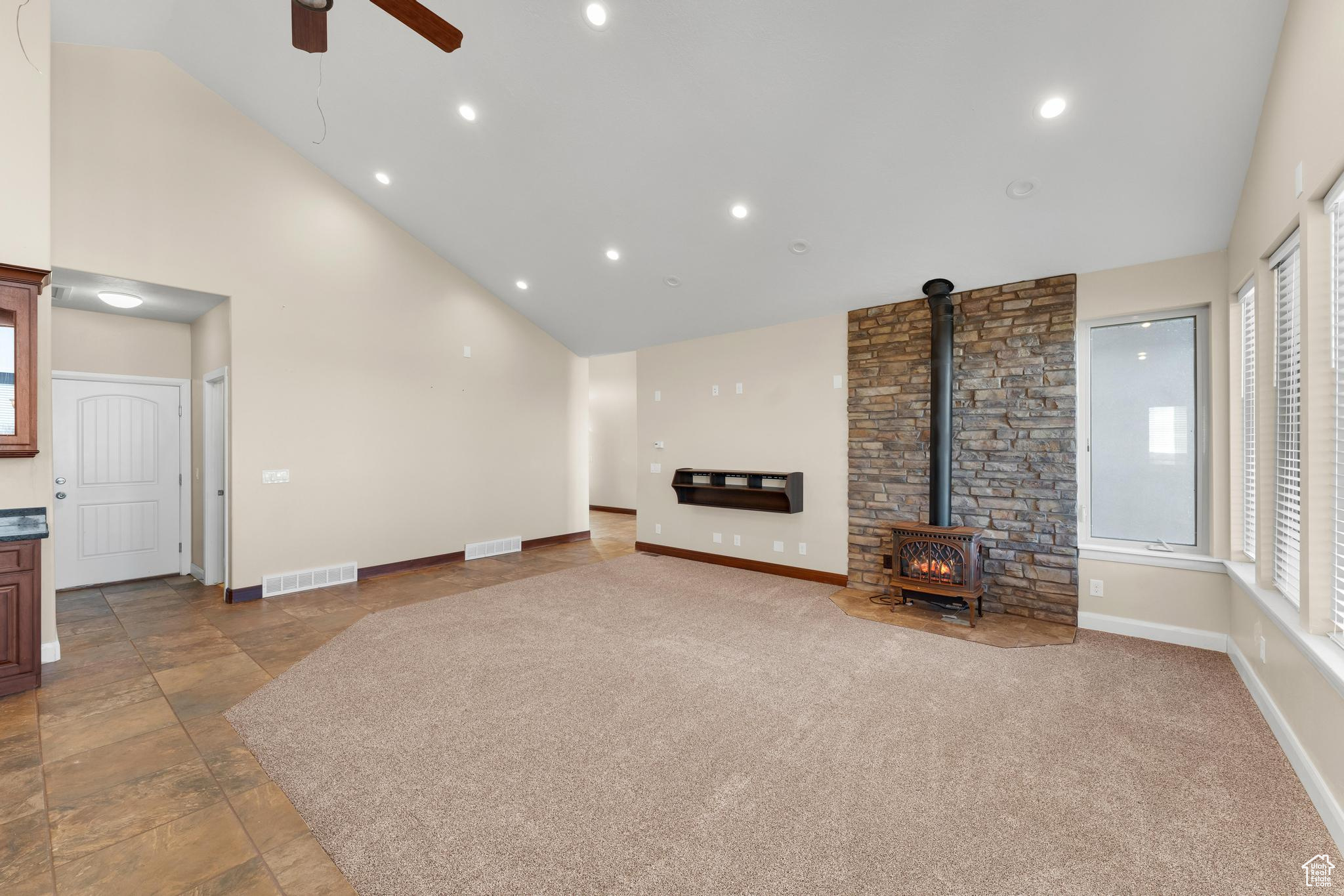 Living room featuring plenty of natural light, lofted ceiling, ceiling fan, light tile floors, and a wood stove