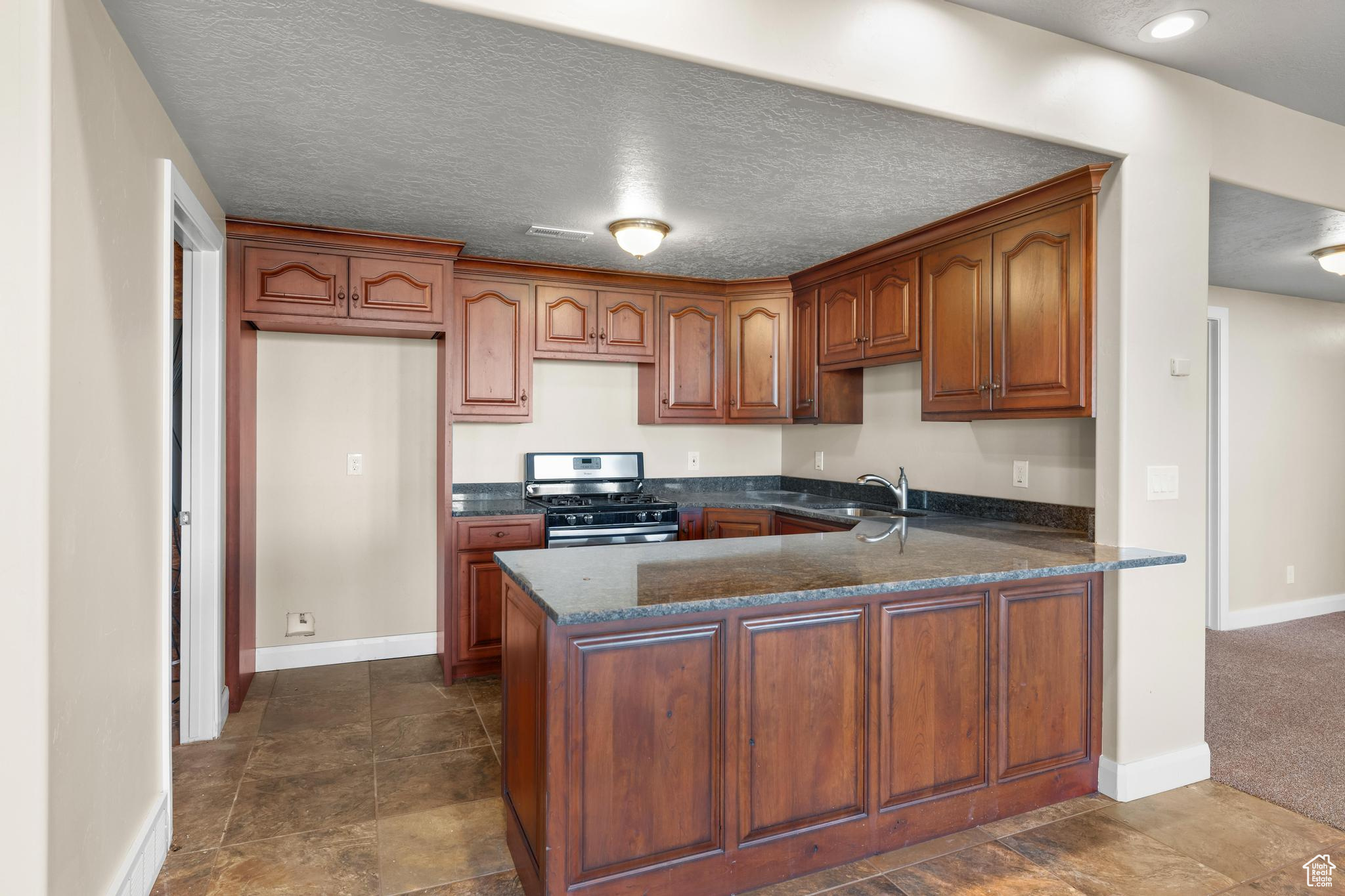 Kitchen with sink, a textured ceiling, kitchen peninsula, and stainless steel range with gas stovetop