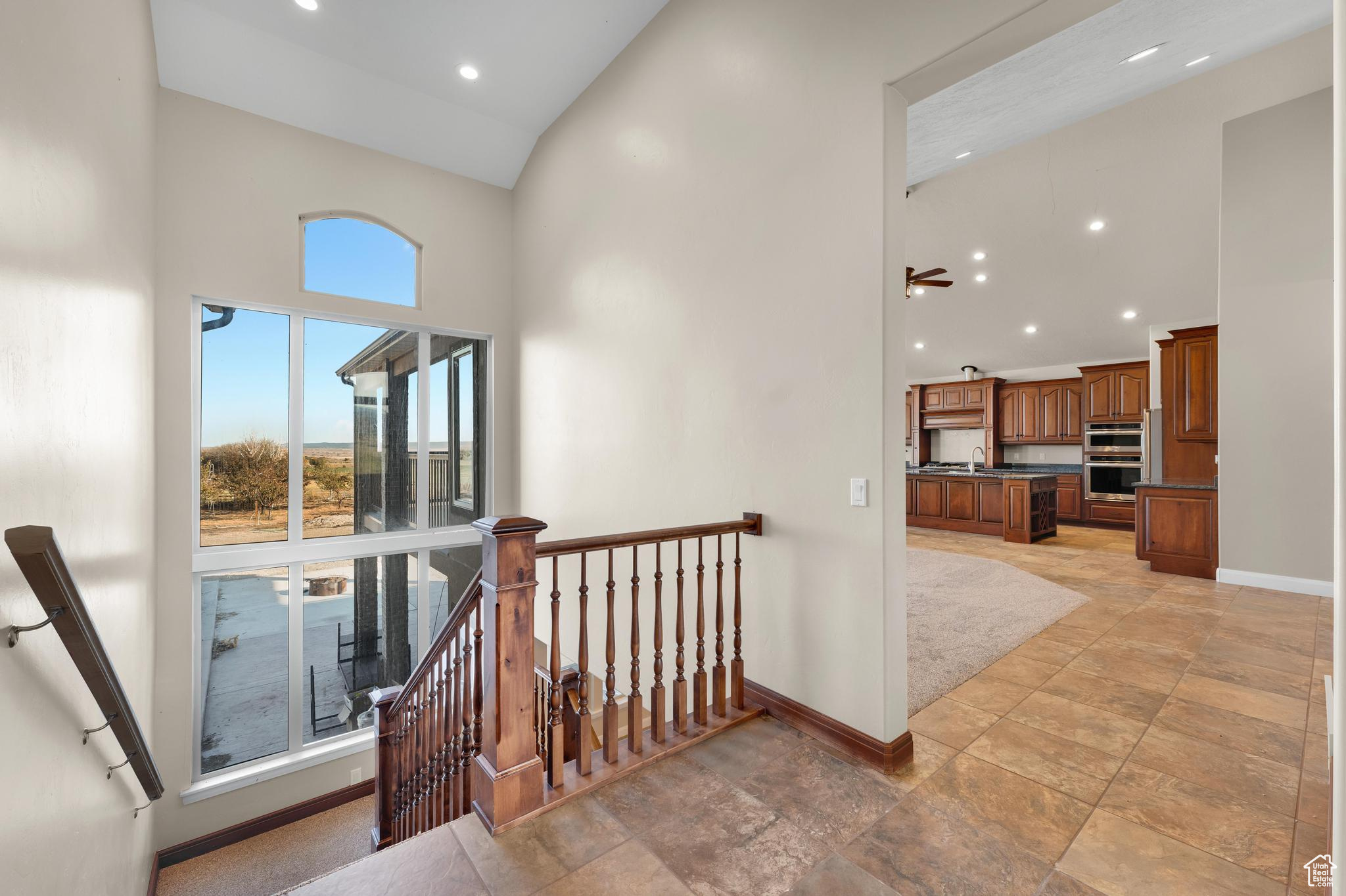 Stairway featuring ceiling fan, light tile flooring, sink, and high vaulted ceiling