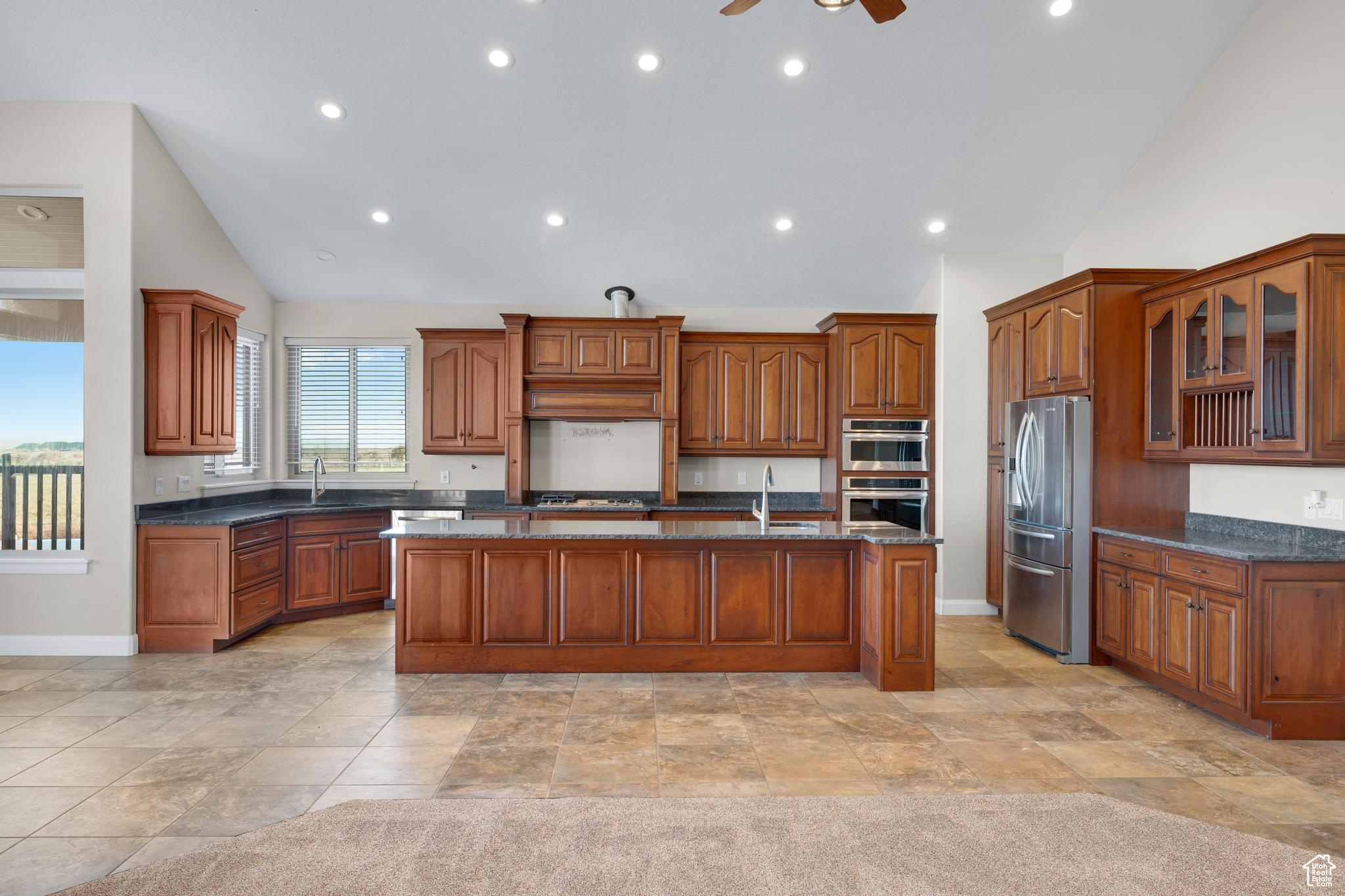 Kitchen featuring ceiling fan, an island with sink, dark stone counters, and appliances with stainless steel finishes