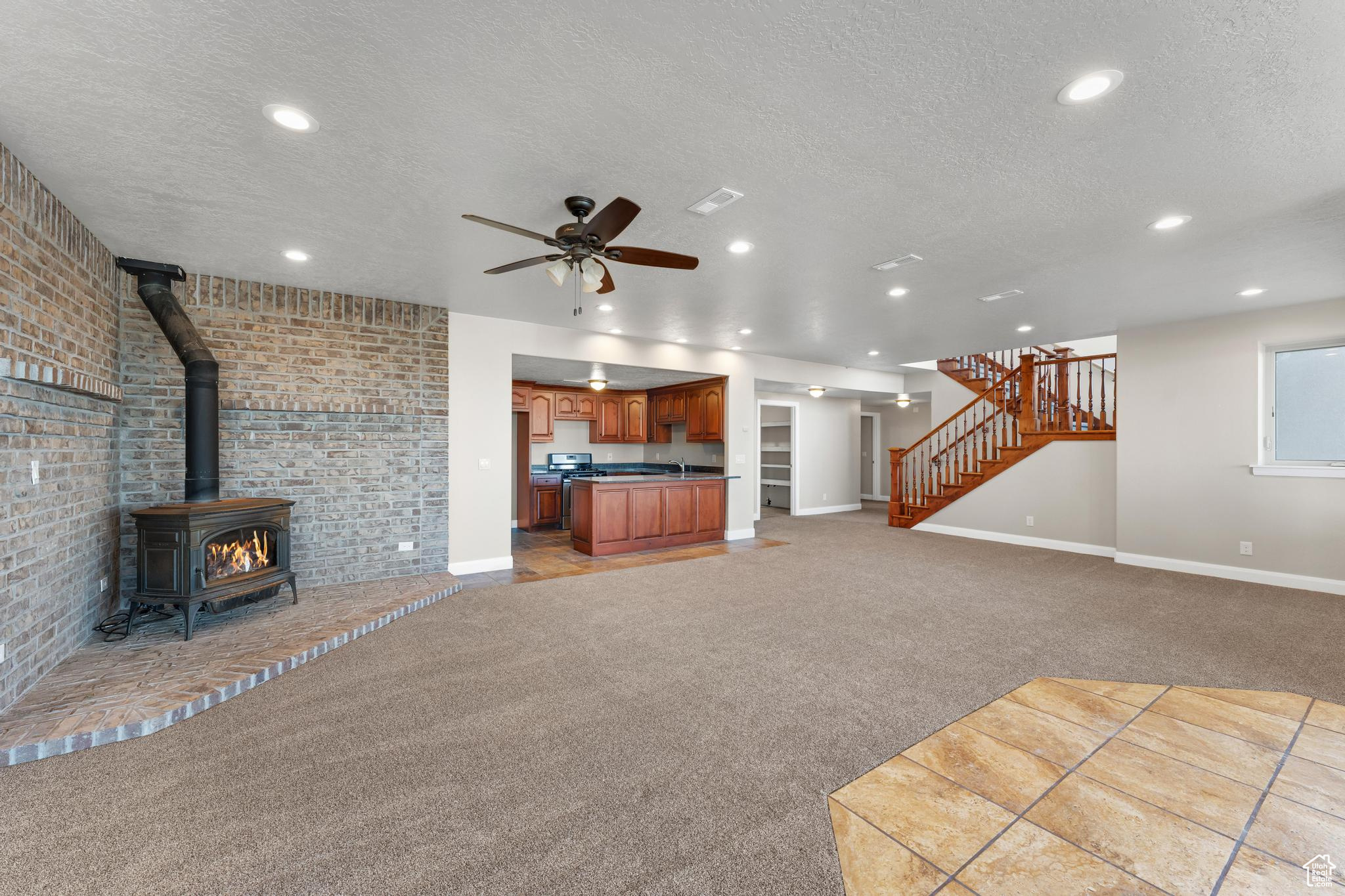 Living room with light carpet, a textured ceiling, ceiling fan, brick wall, and a wood stove