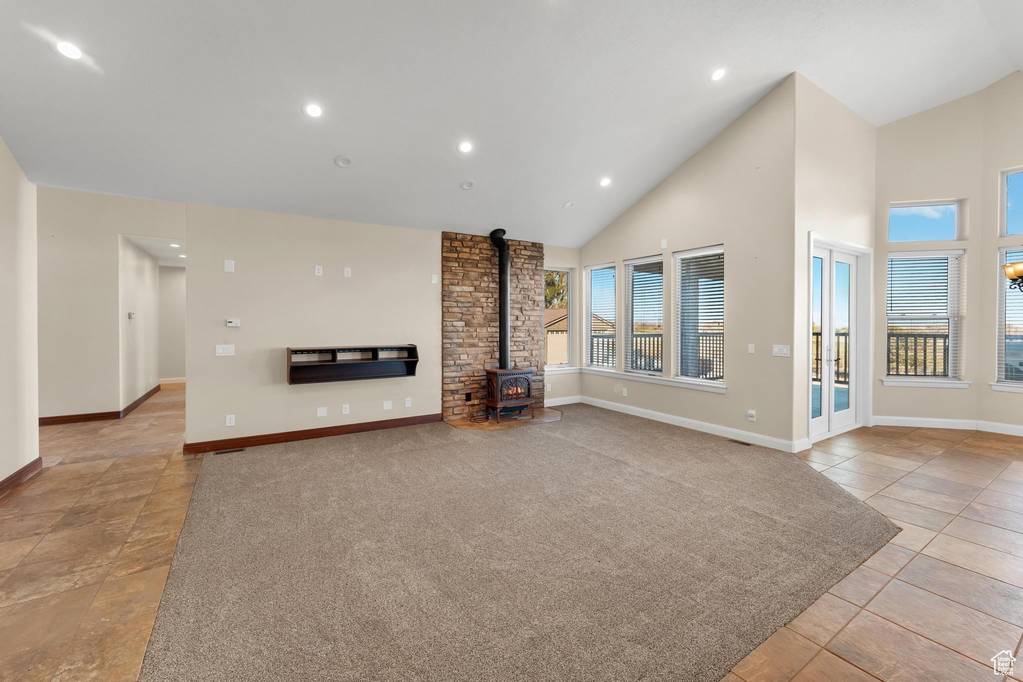 Living room featuring a wood stove, high vaulted ceiling, brick wall, and light tile floors