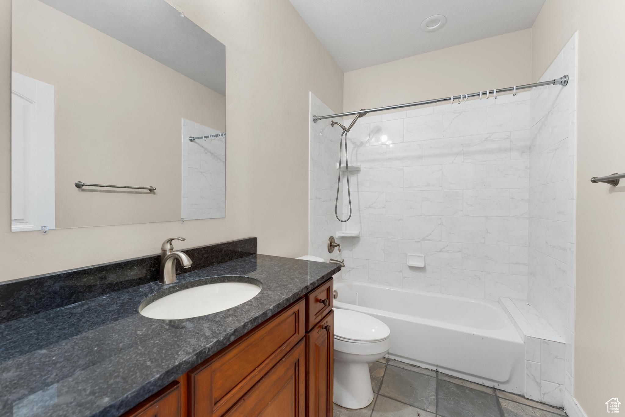 Full bathroom with tiled shower / bath, toilet, vanity with extensive cabinet space, and tile flooring