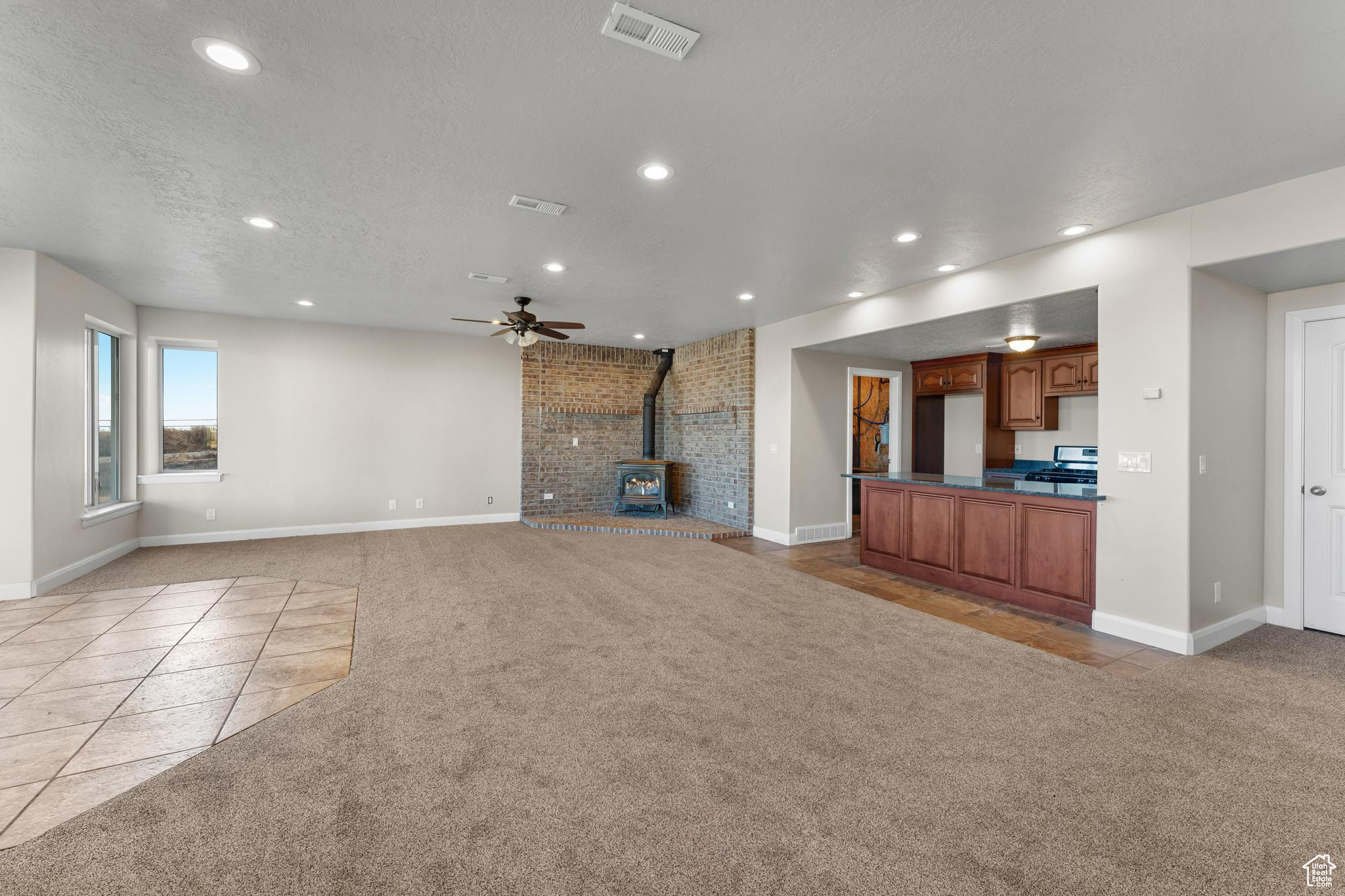 Living room featuring light tile floors, a wood stove, ceiling fan, and a textured ceiling where family and friends could easily gather.