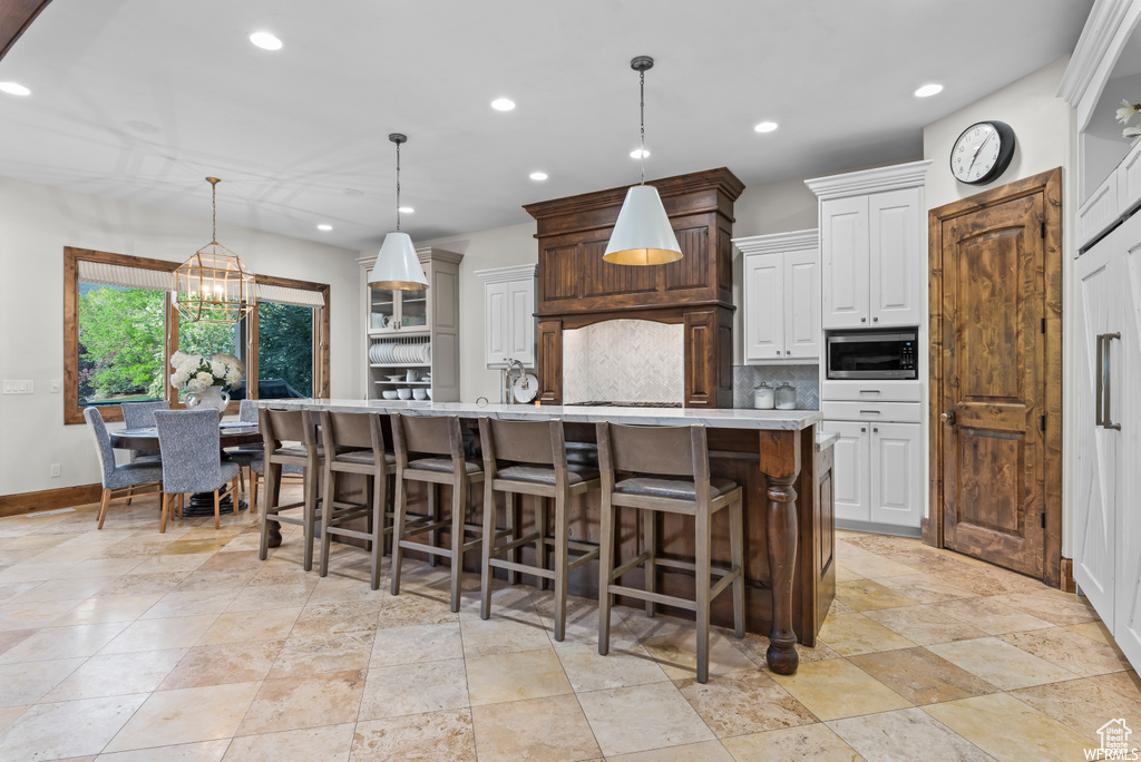 Kitchen featuring hanging light fixtures, stainless steel microwave, a large island, and tasteful backsplash